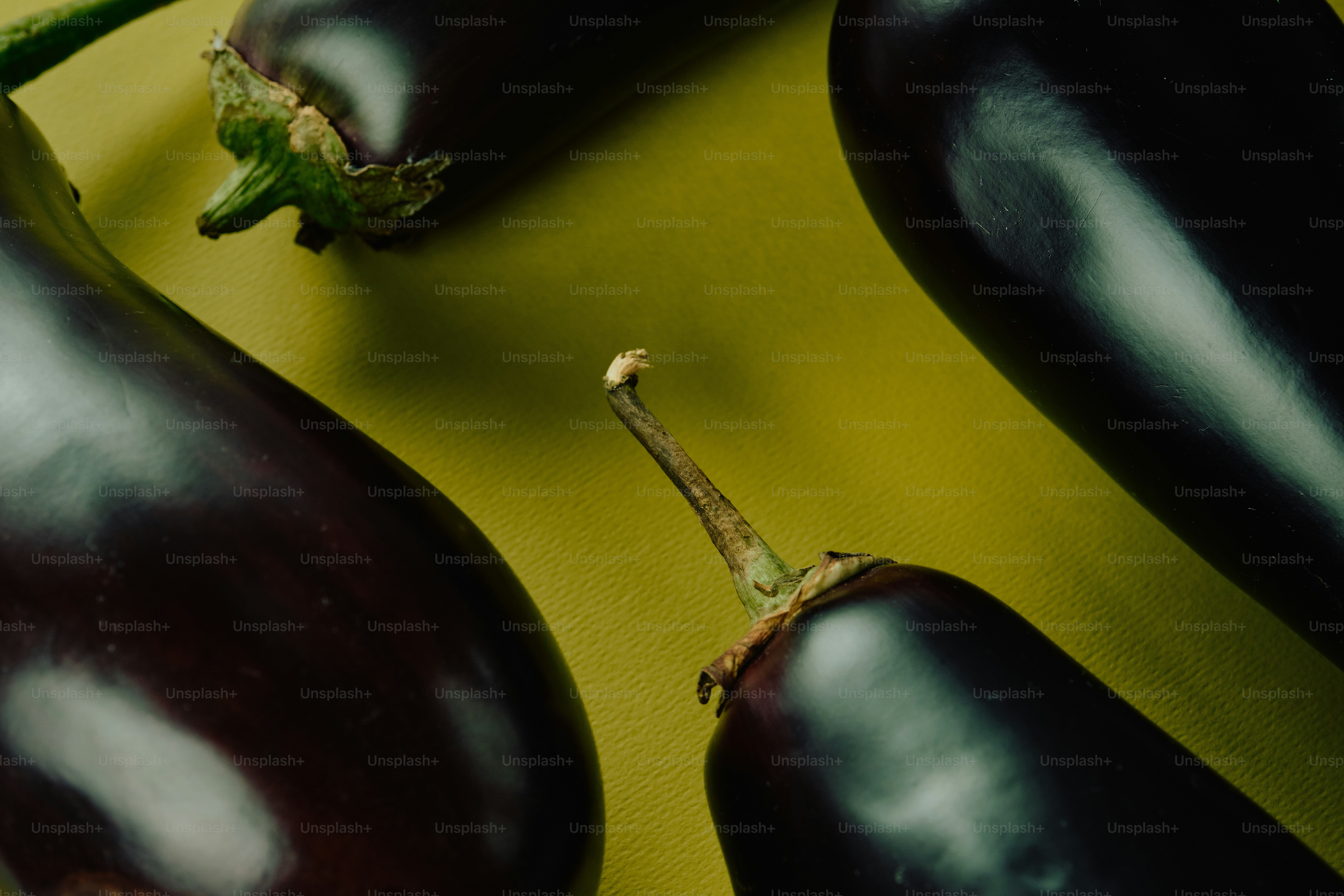 Three dark purple eggplants arranged on a textured yellow surface