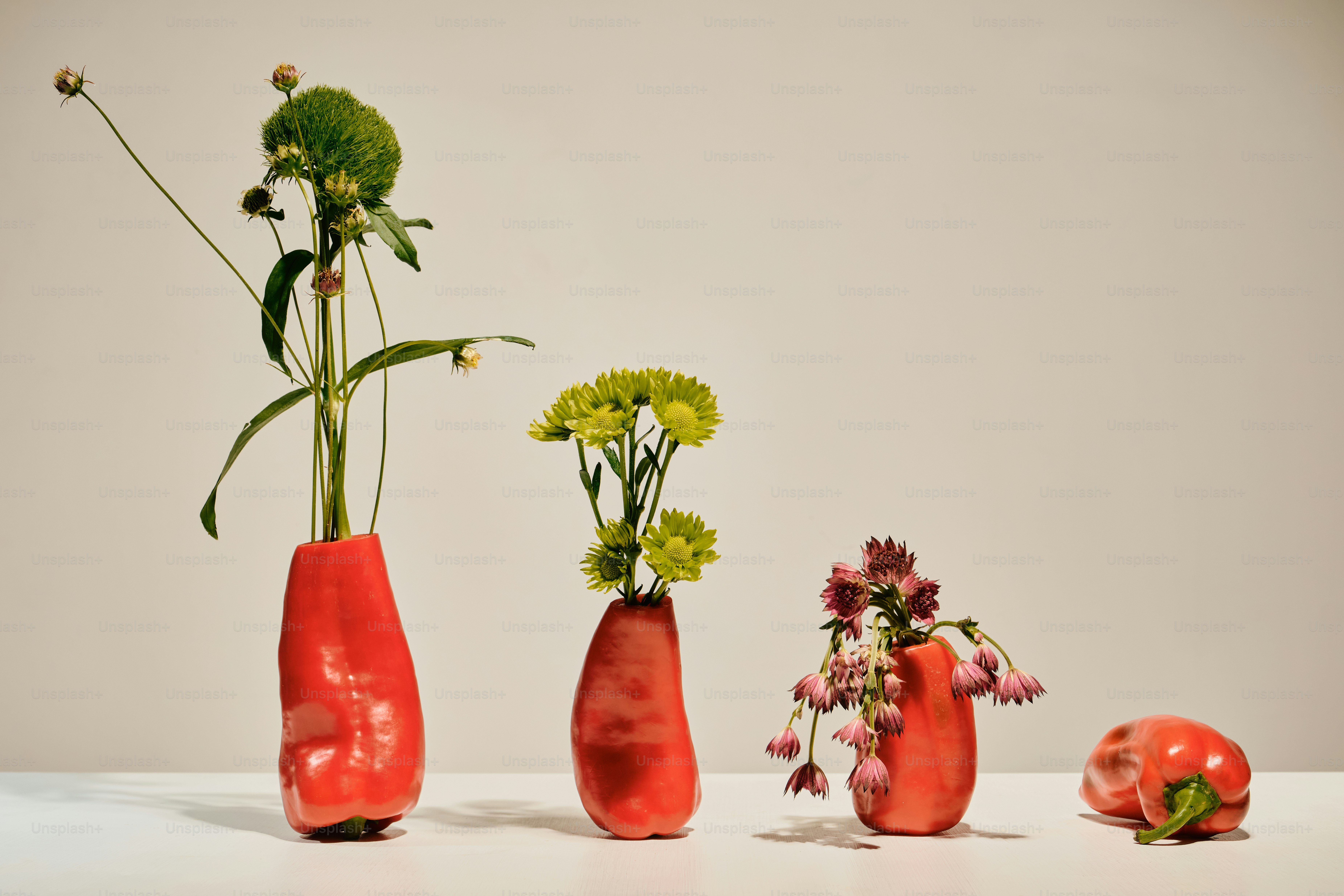 Three red bell peppers used as vases for flowers on a white surface