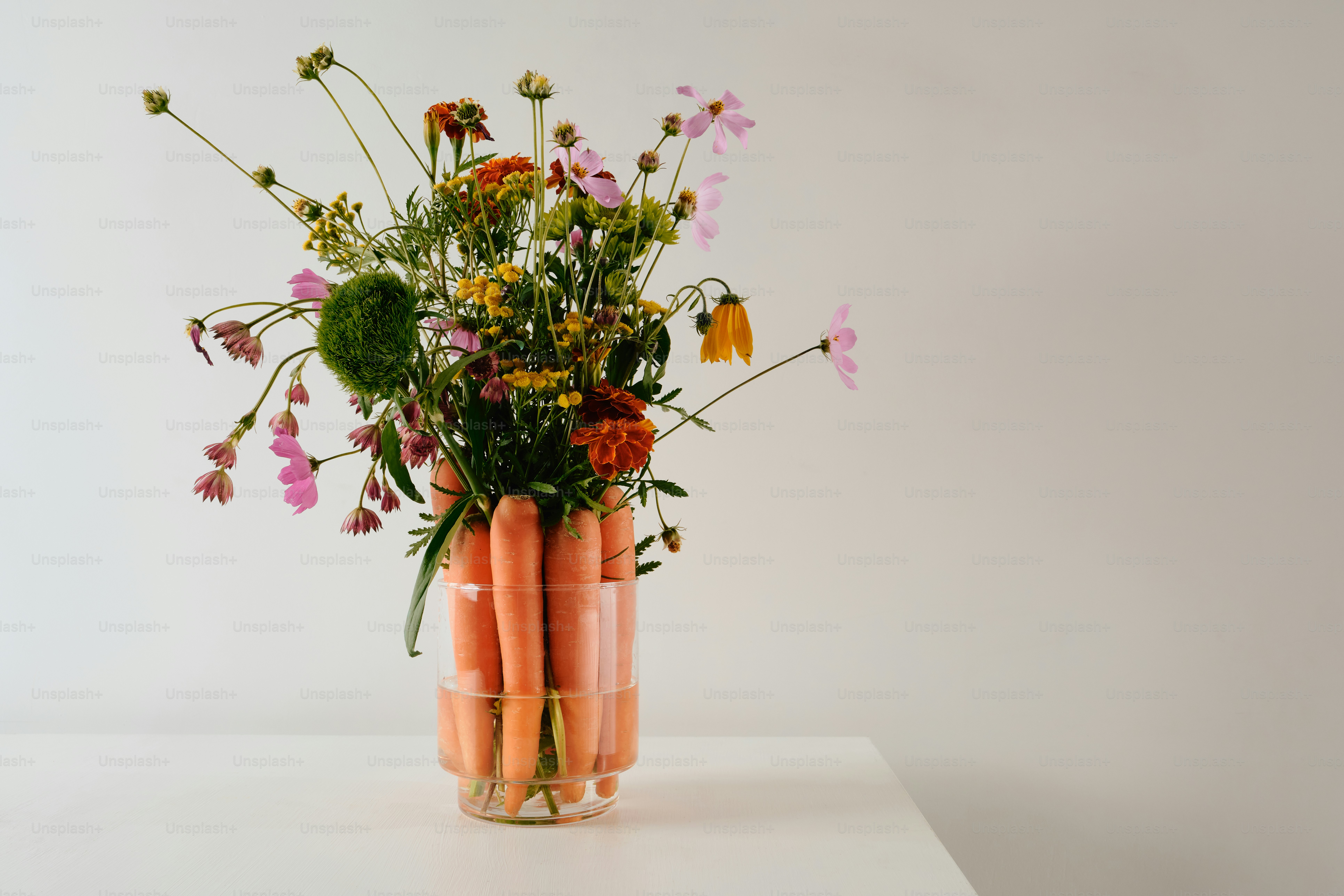 A bouquet of wildflowers in a glass vase filled with orange carrots