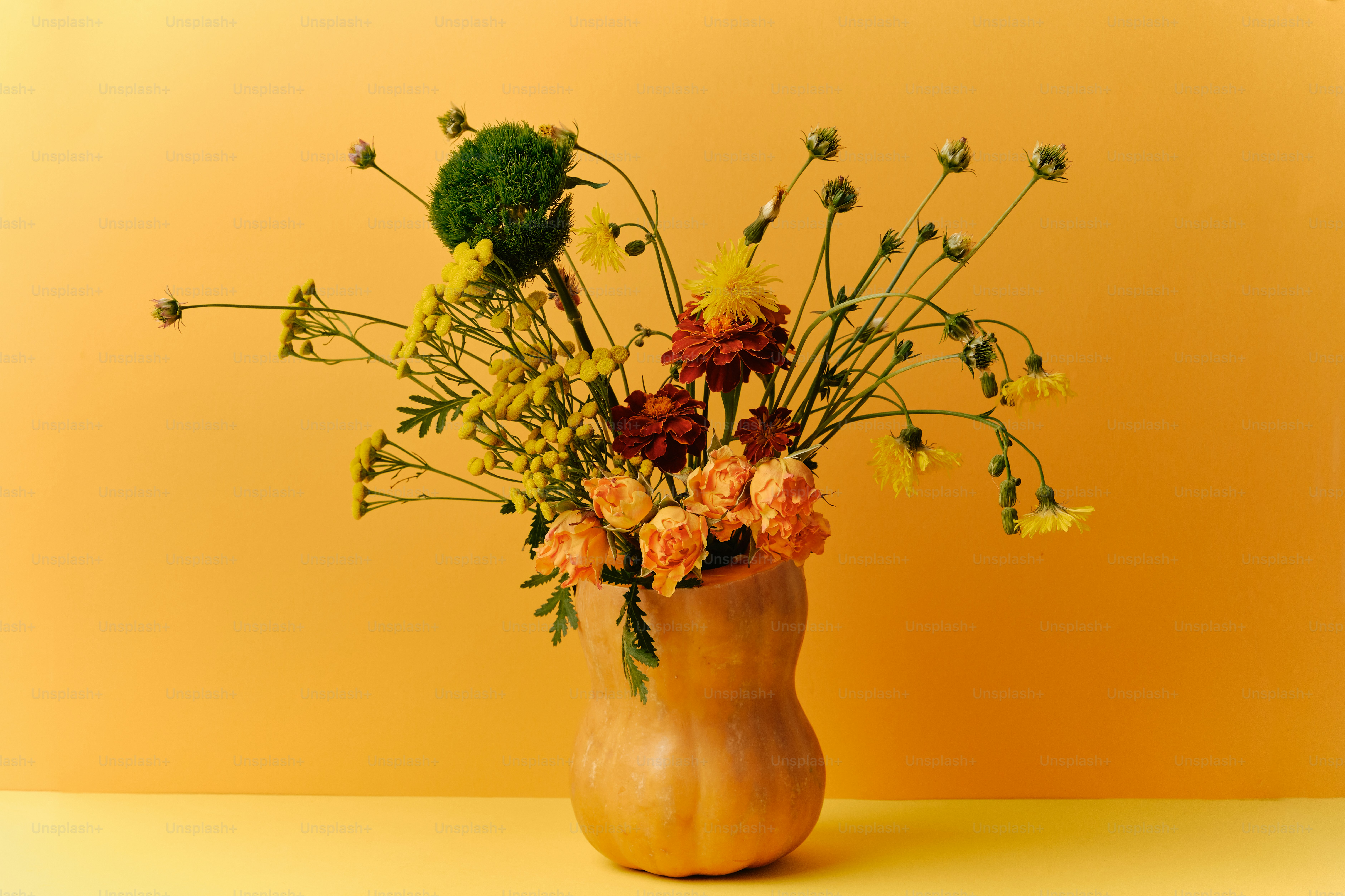 A bouquet of yellow and orange flowers in a hollowed butternut squash vase