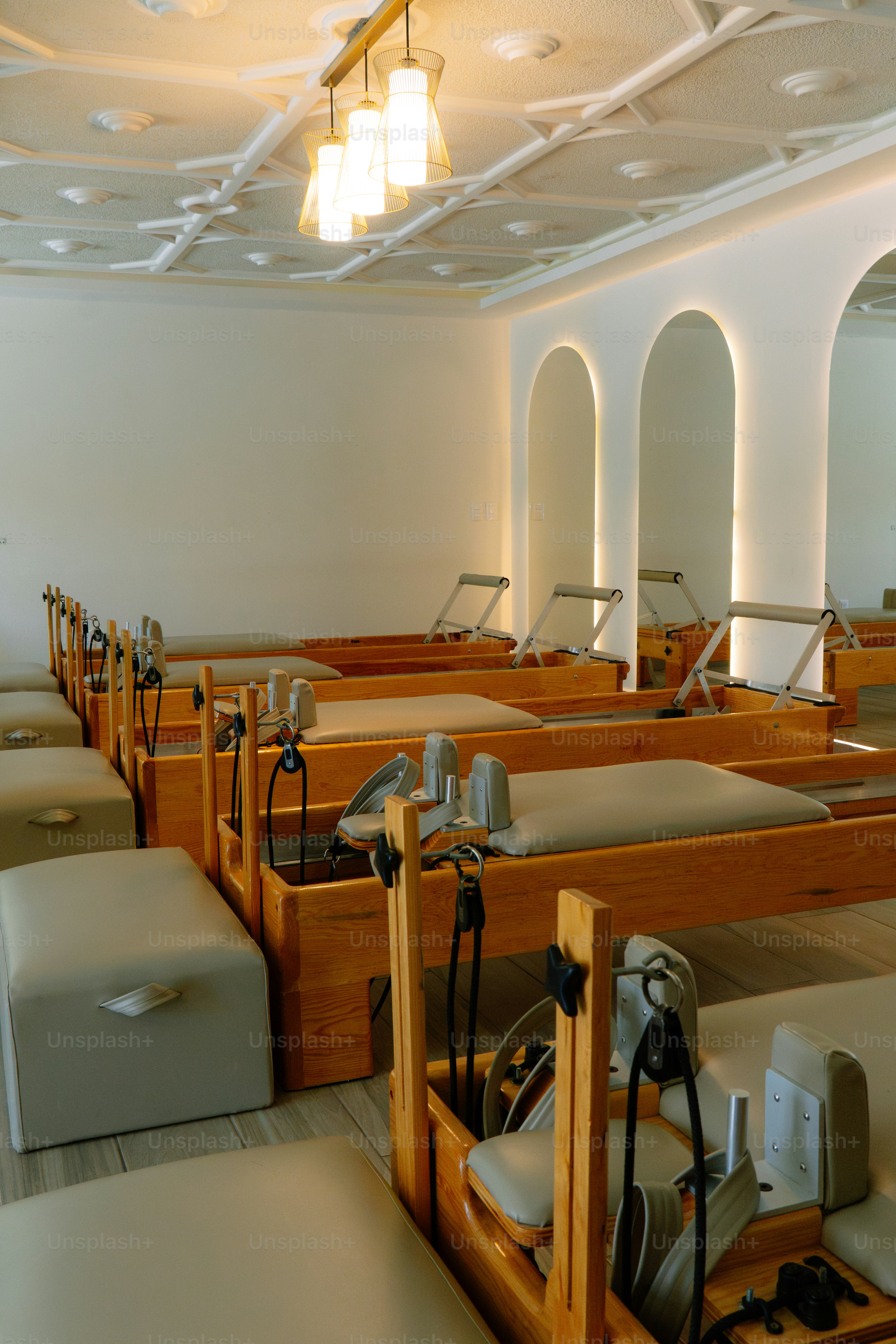 A row of wooden pilates reformers in a bright studio with arched mirrors
