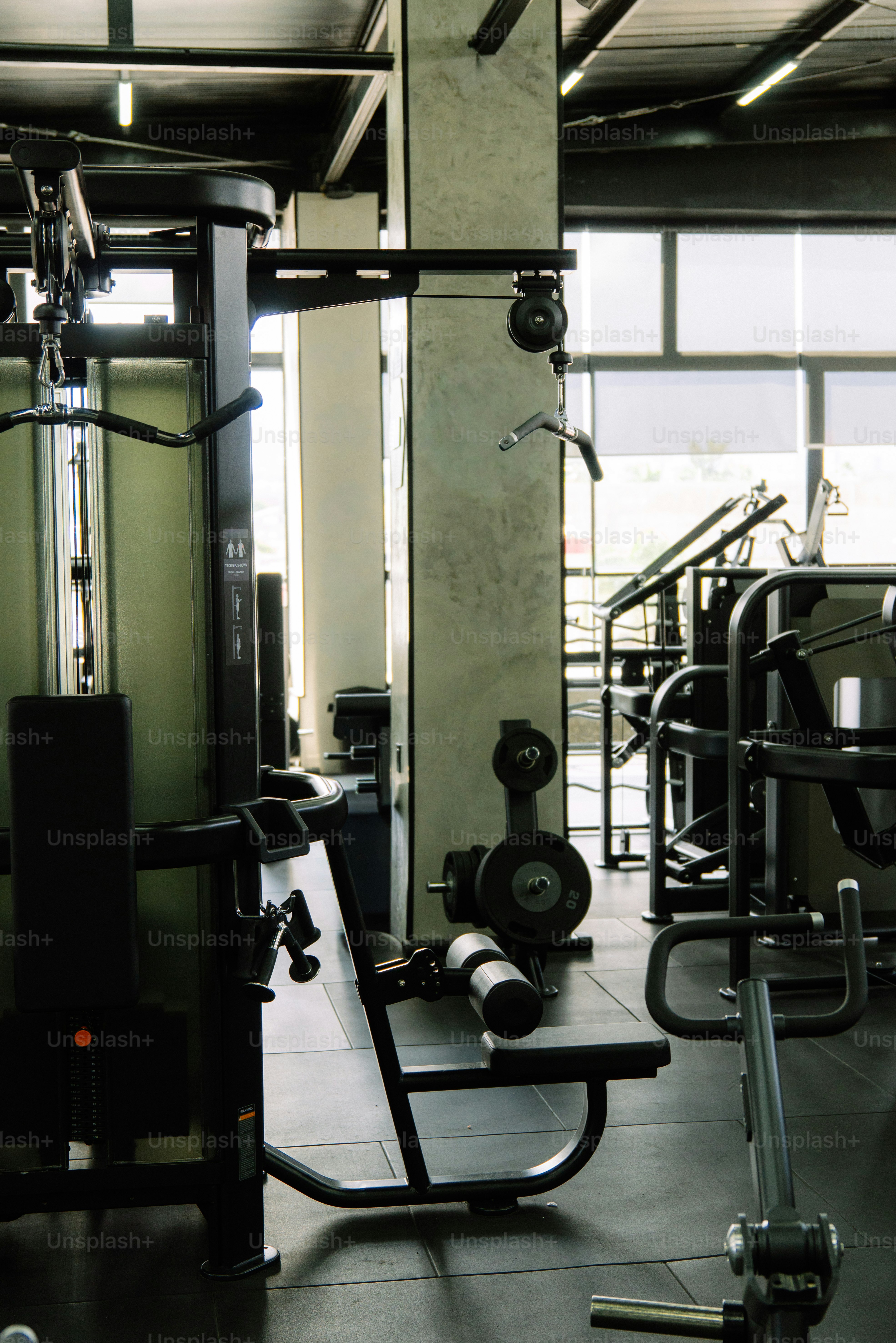 Black exercise machines and weight plates in a modern gym with large windows