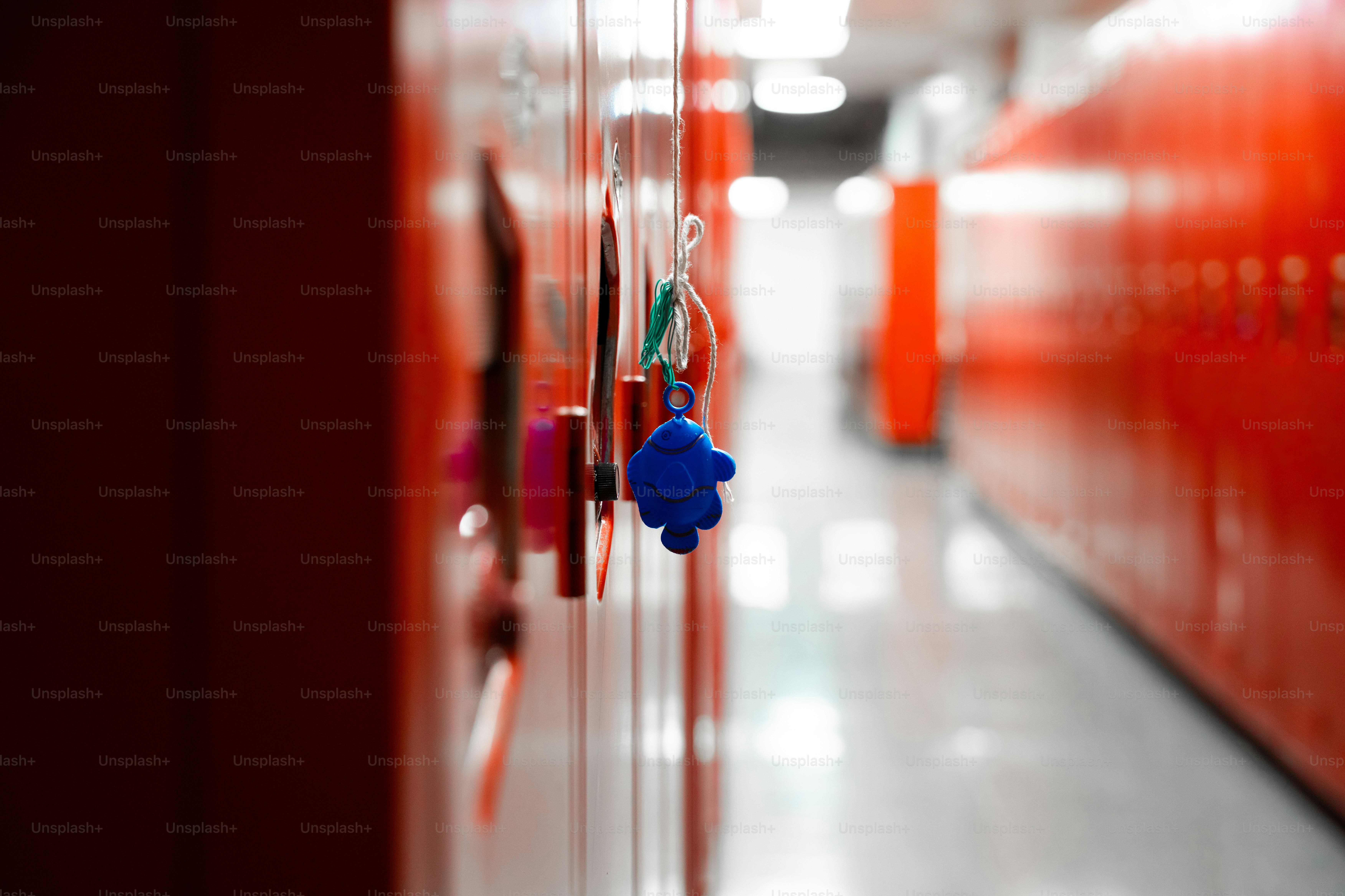 A blue plastic fish charm hanging from a string on a red locker