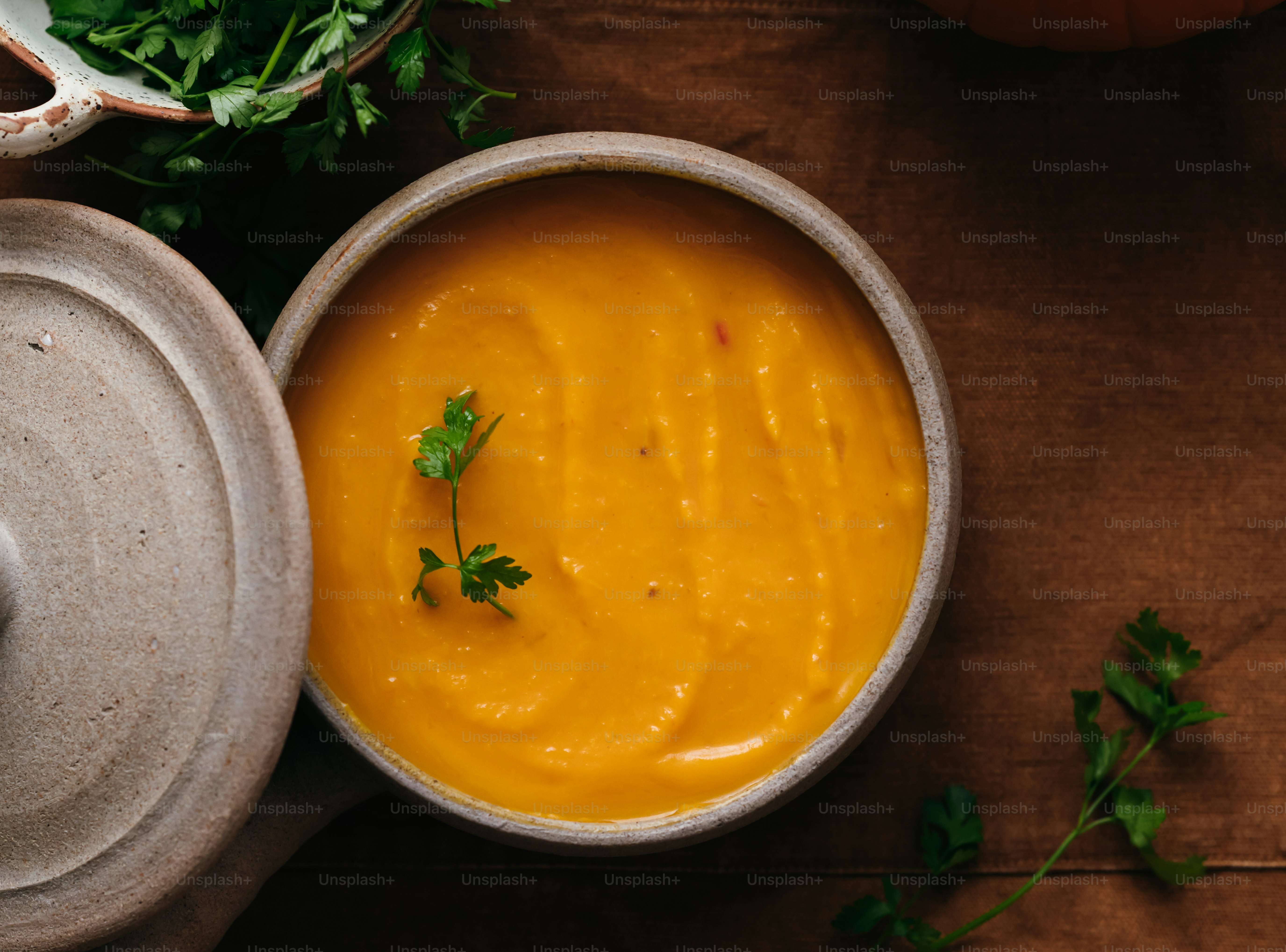 Un bol de soupe à l’orange garni de persil sur un tissu brun foncé