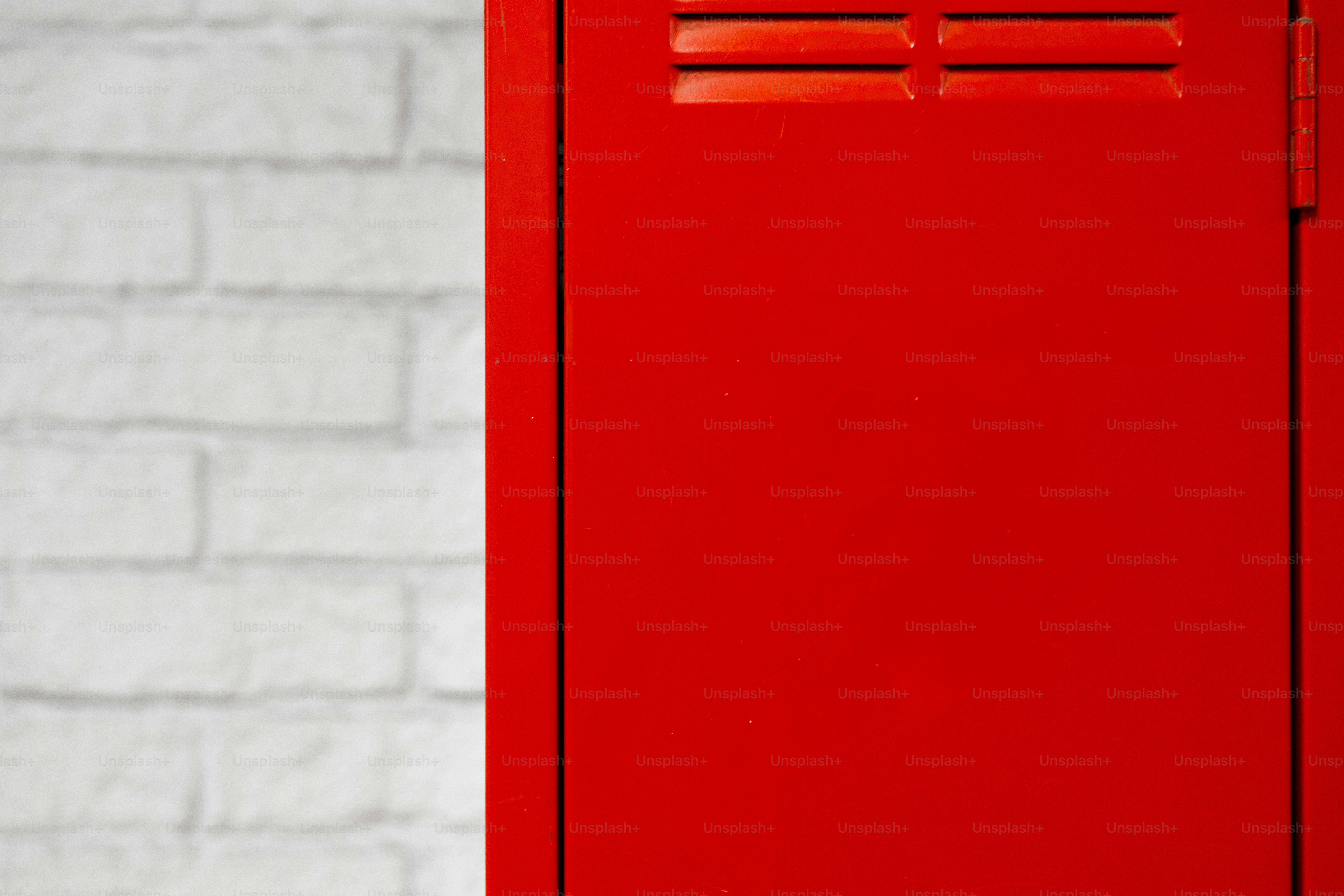 A bright red metal locker door against a white painted brick wall
