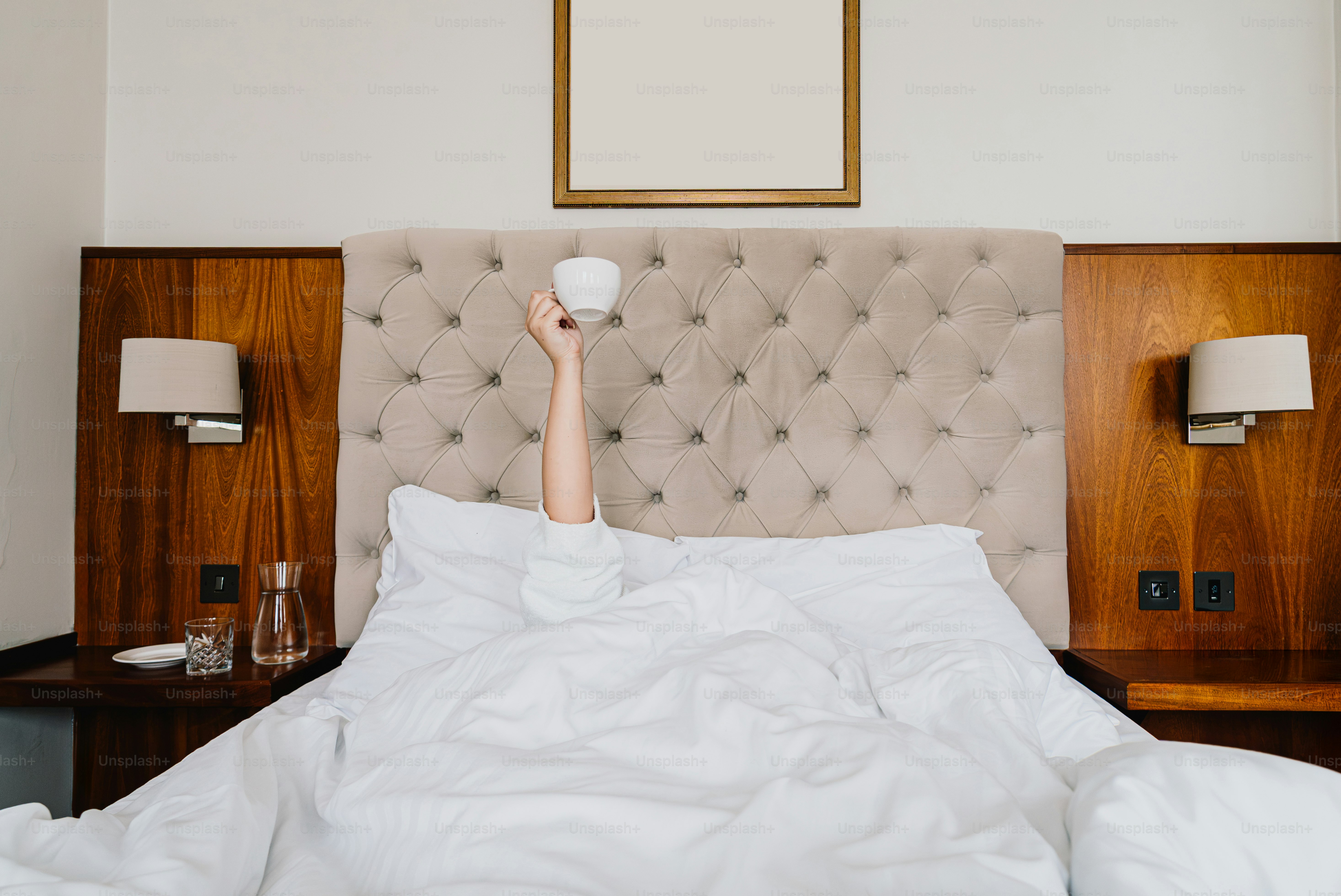 A person in bed holding a white coffee cup up into the air