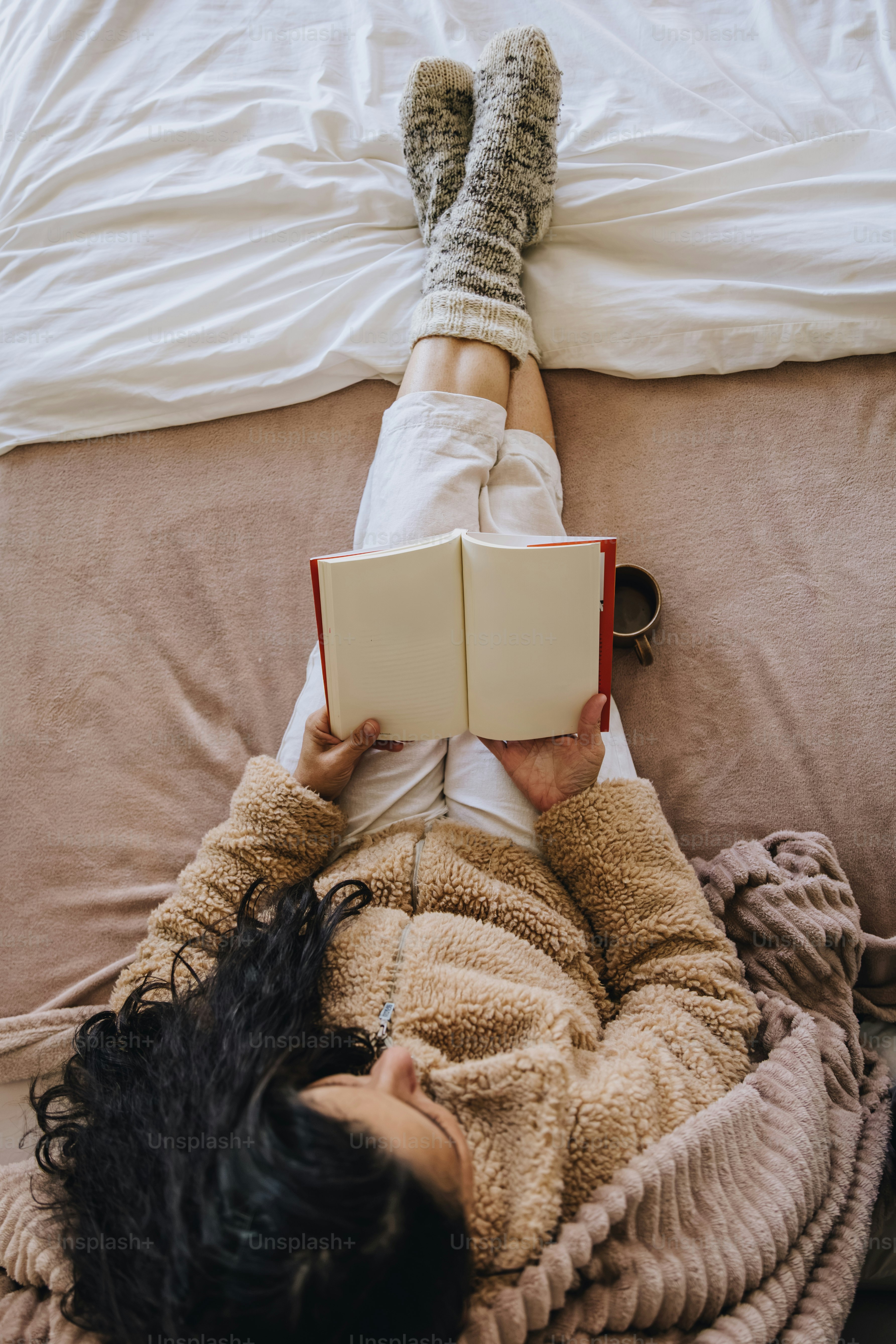 A person in a fleece jacket reading a book on a bed