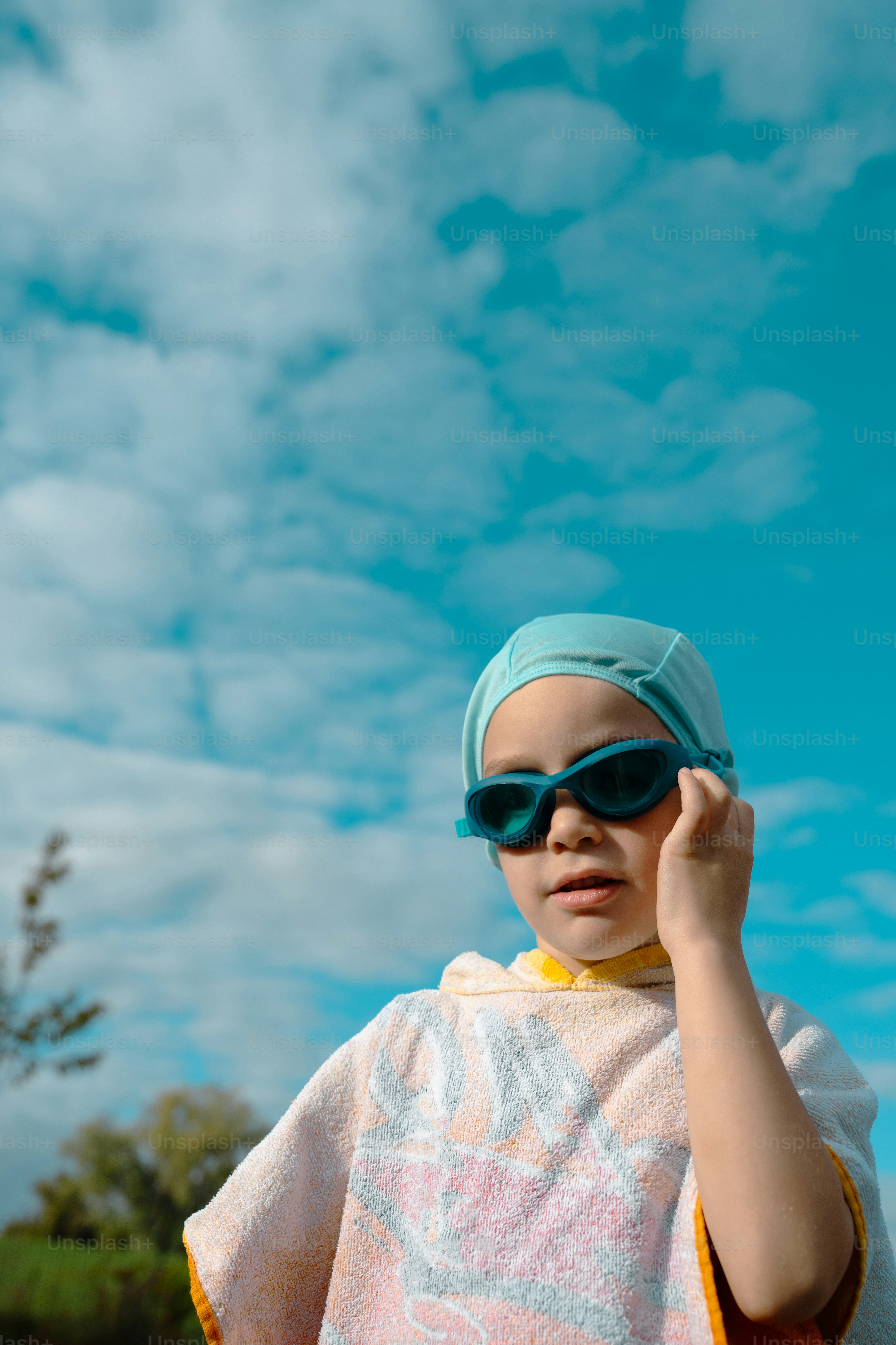 A child in a swim cap and goggles wearing a towel poncho outdoors