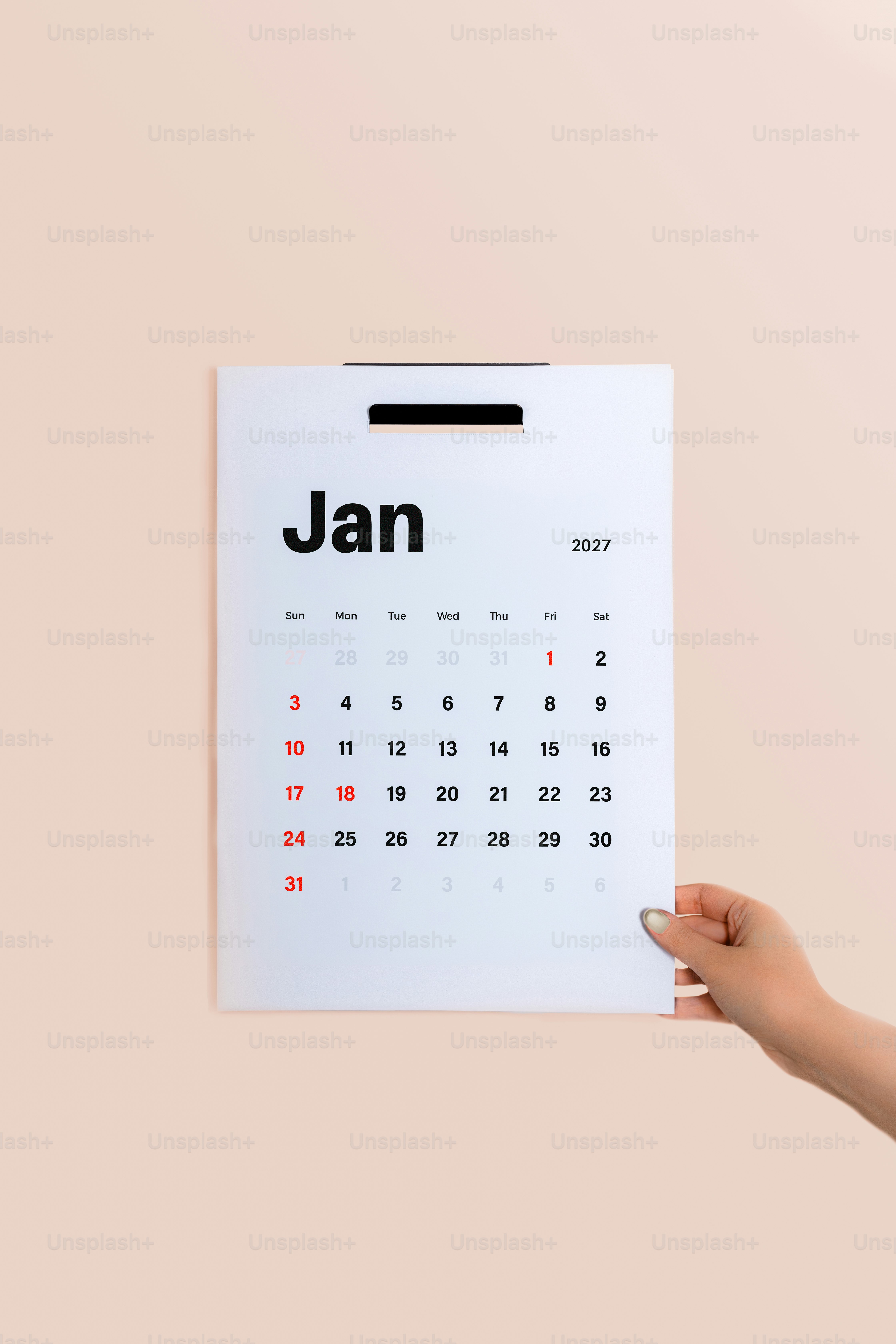 A hand holding a January 2027 calendar page against a light beige background