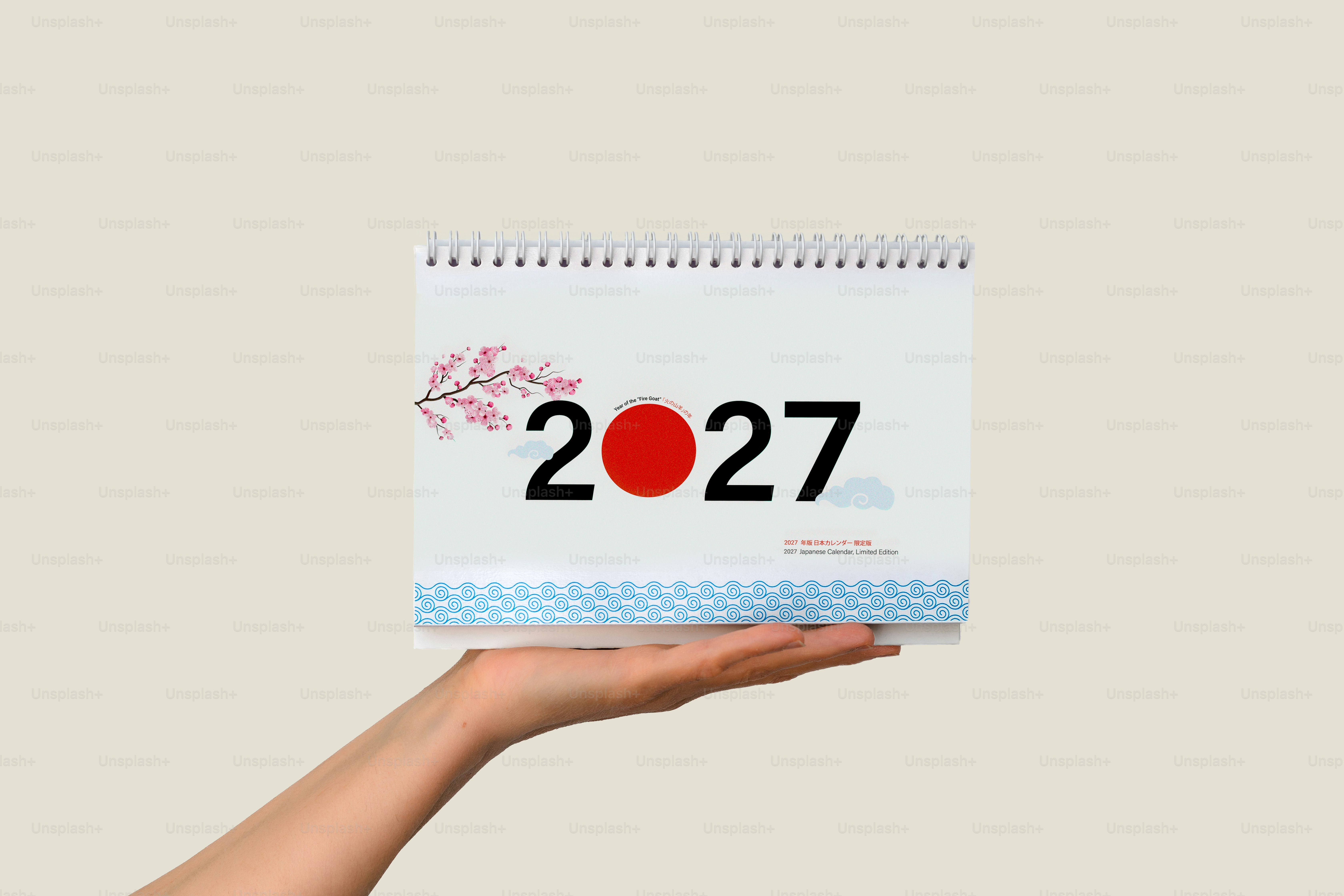 A hand holding a 2027 desk calendar with cherry blossom and wave illustrations