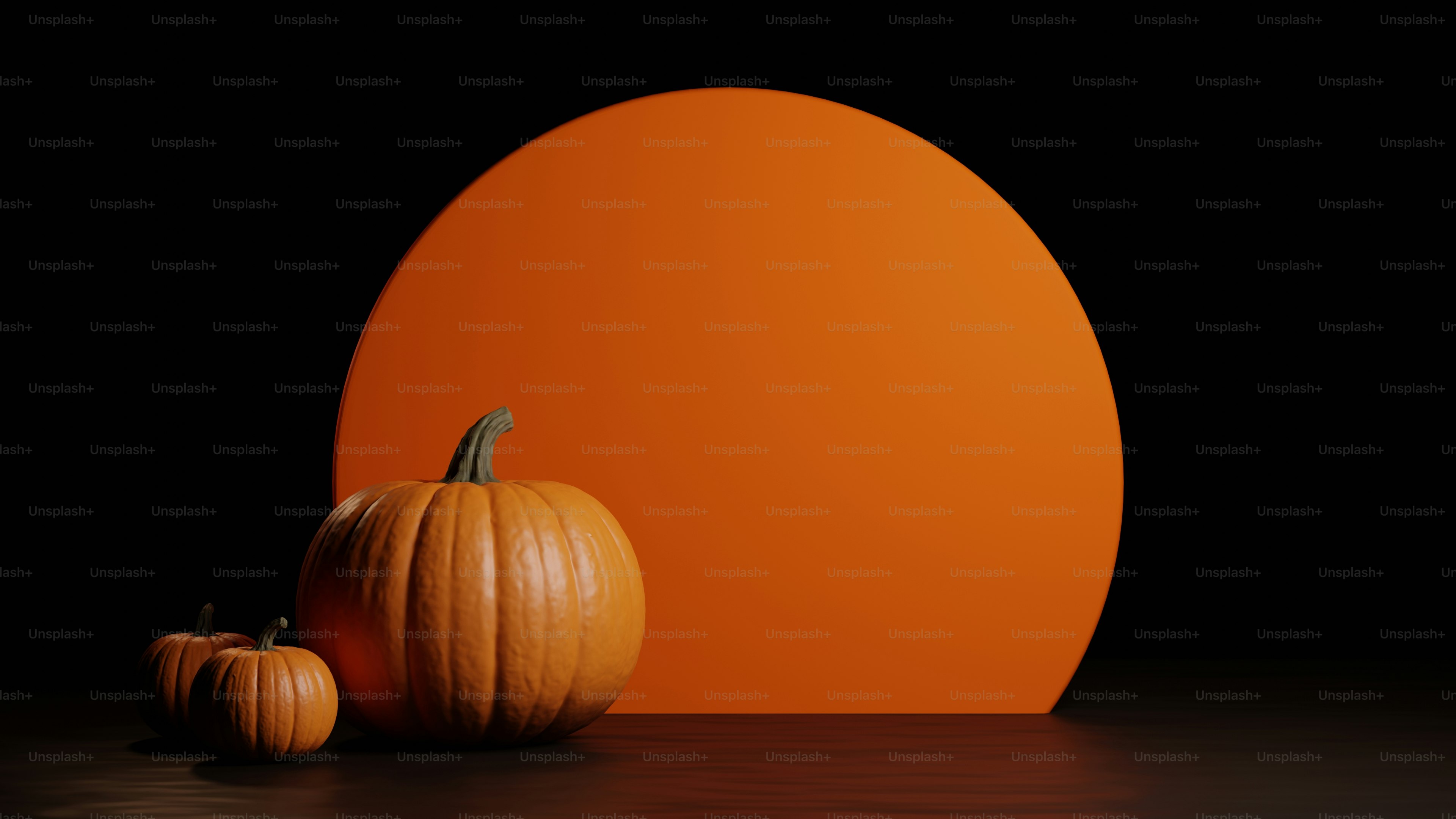 Tres calabazas naranjas delante de un gran círculo naranja sobre una superficie oscura