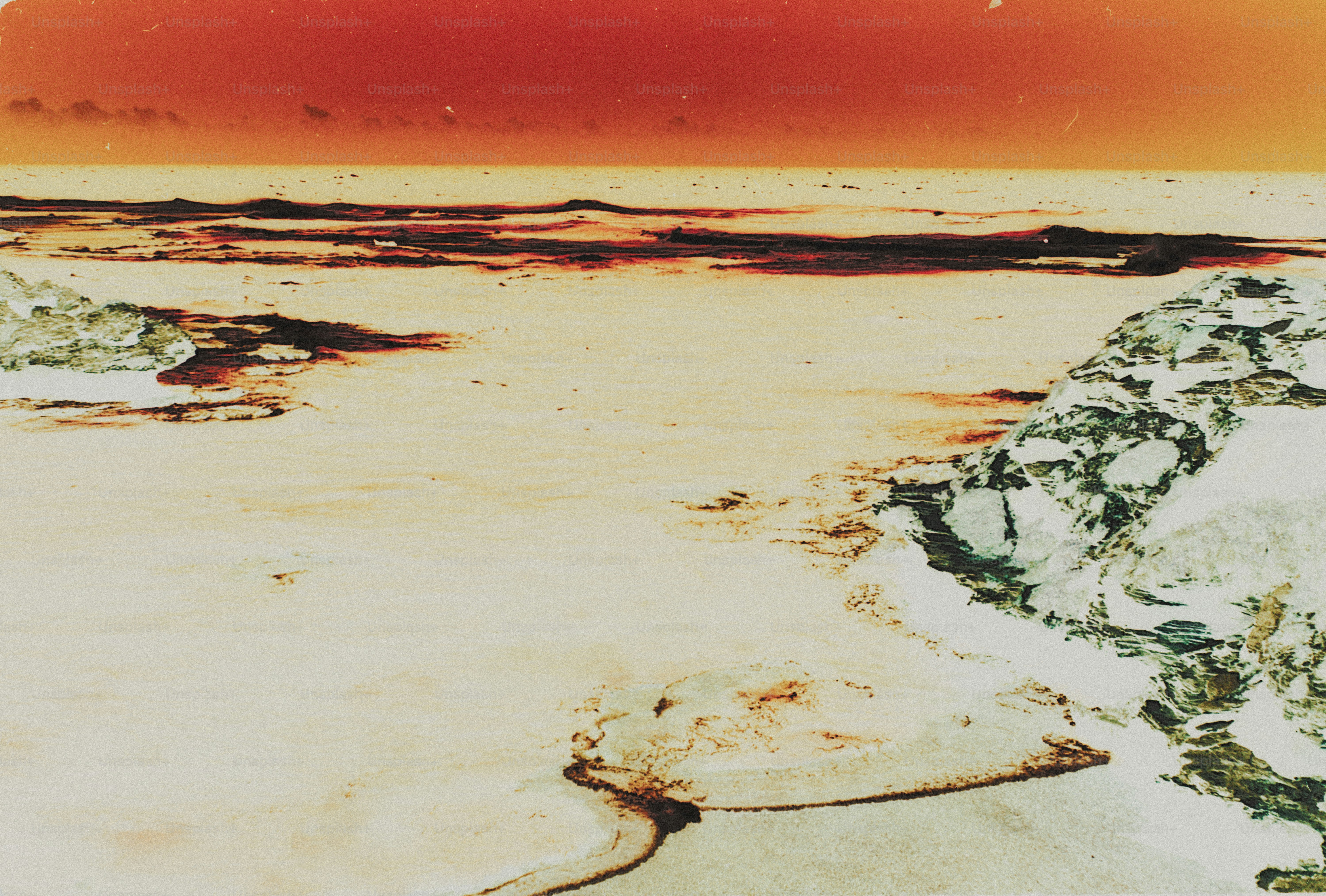 A rocky shoreline under a warm orange sky with dark textured clouds