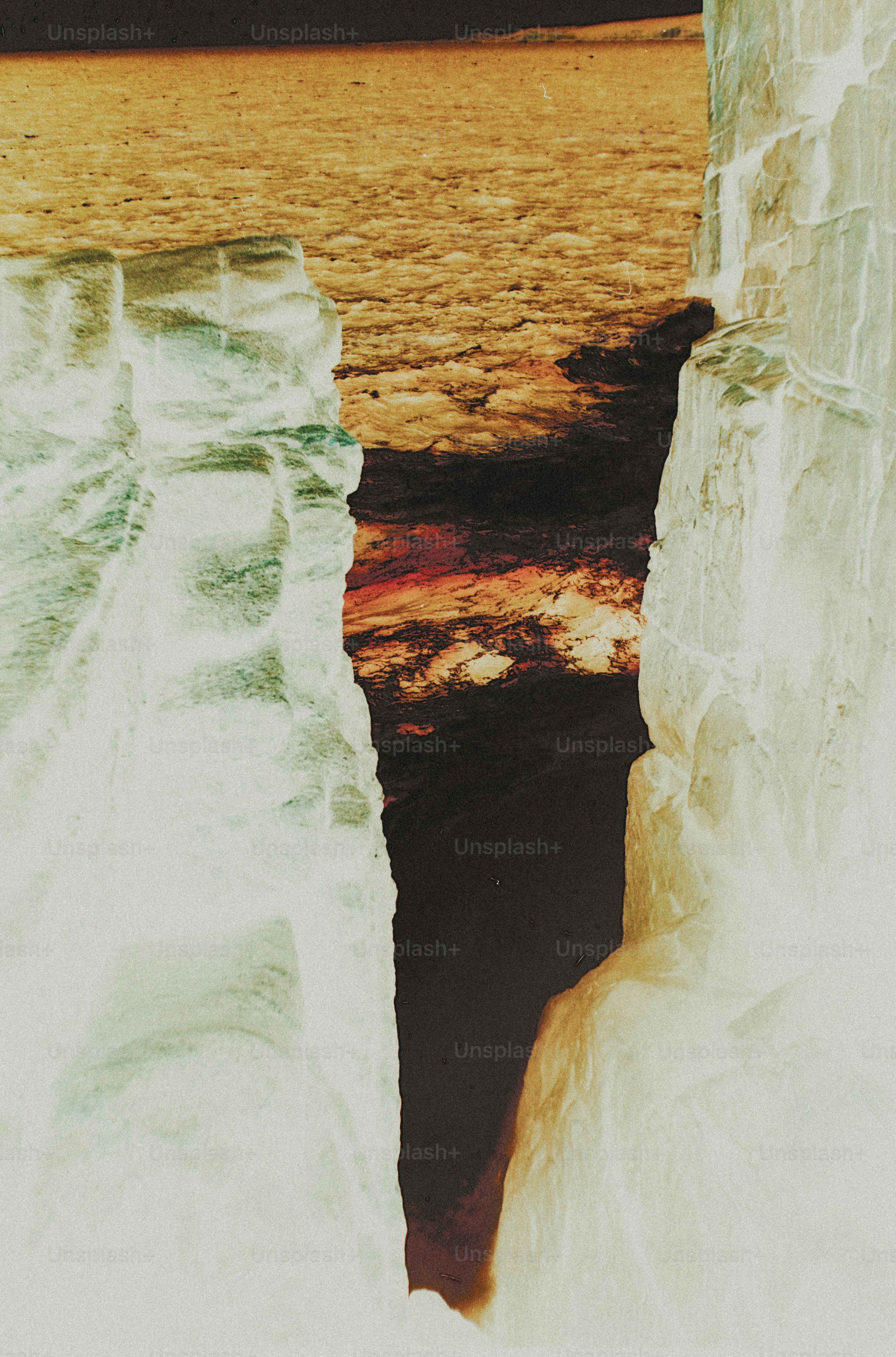 A narrow dark crevice between two tall pale rock formations above water