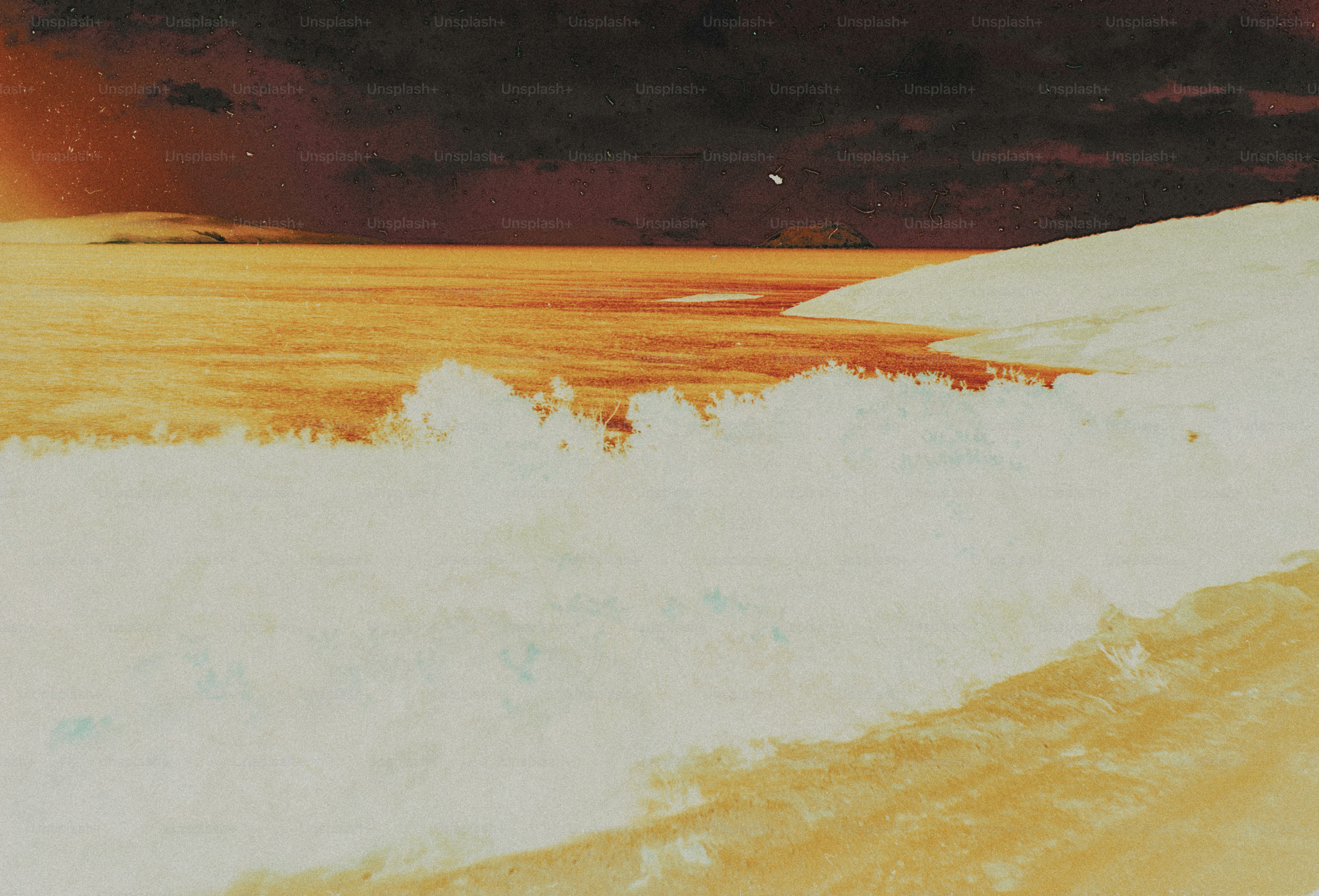 White ocean waves crashing onto a sandy beach under a dark sky