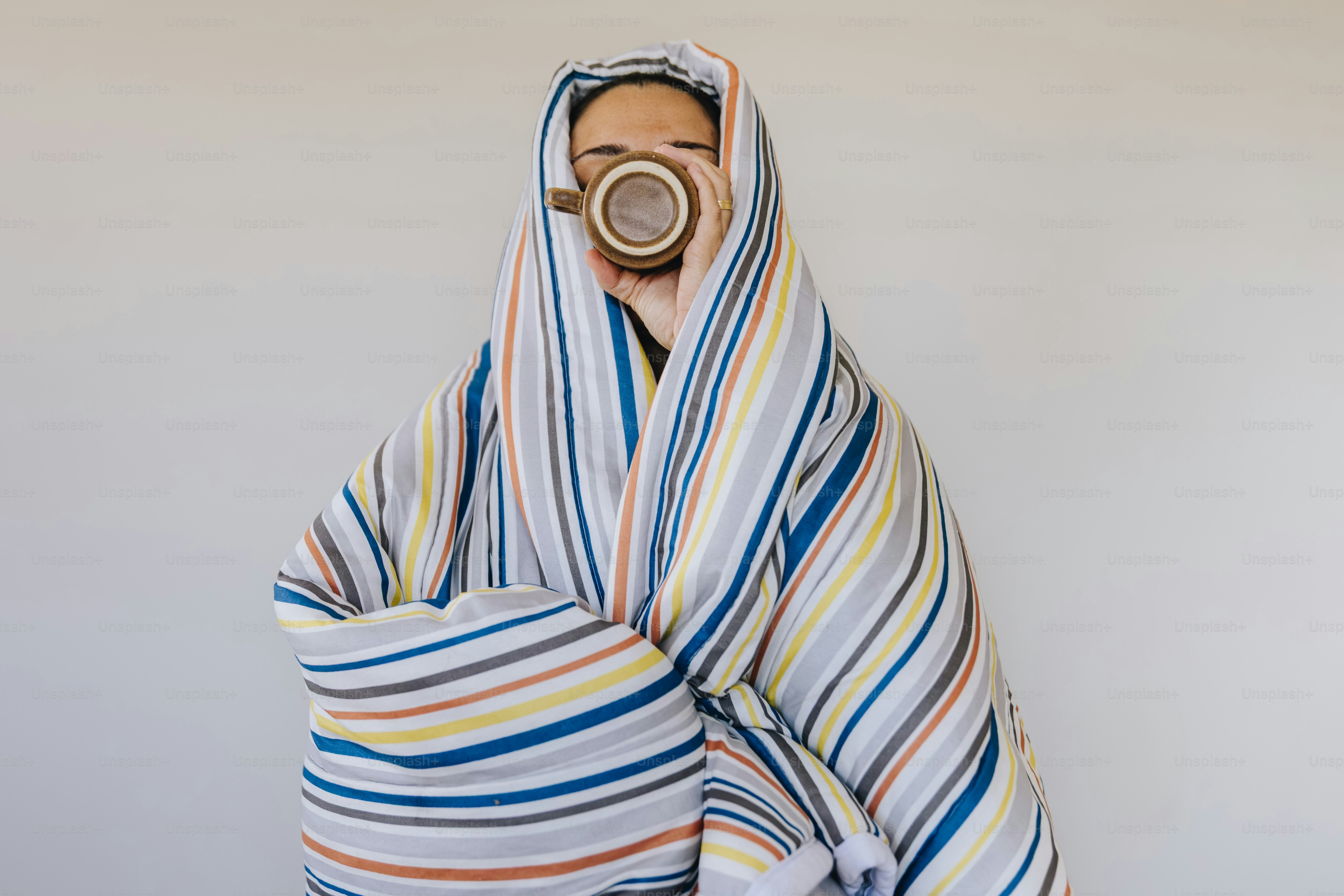 A person wrapped in a striped blanket holding a brown ceramic mug