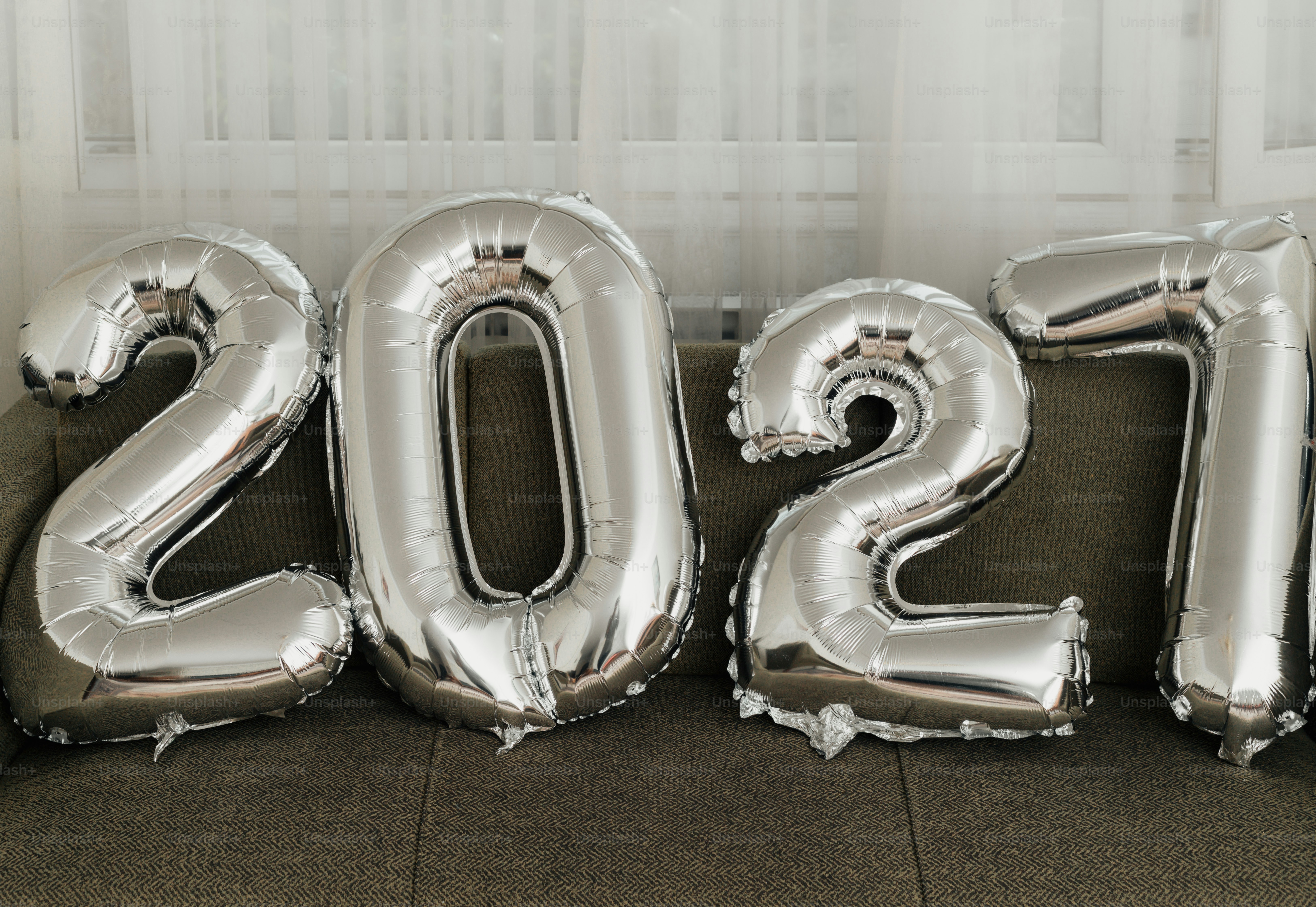 Large silver foil balloons shaped as the number 2027 on a grey sofa