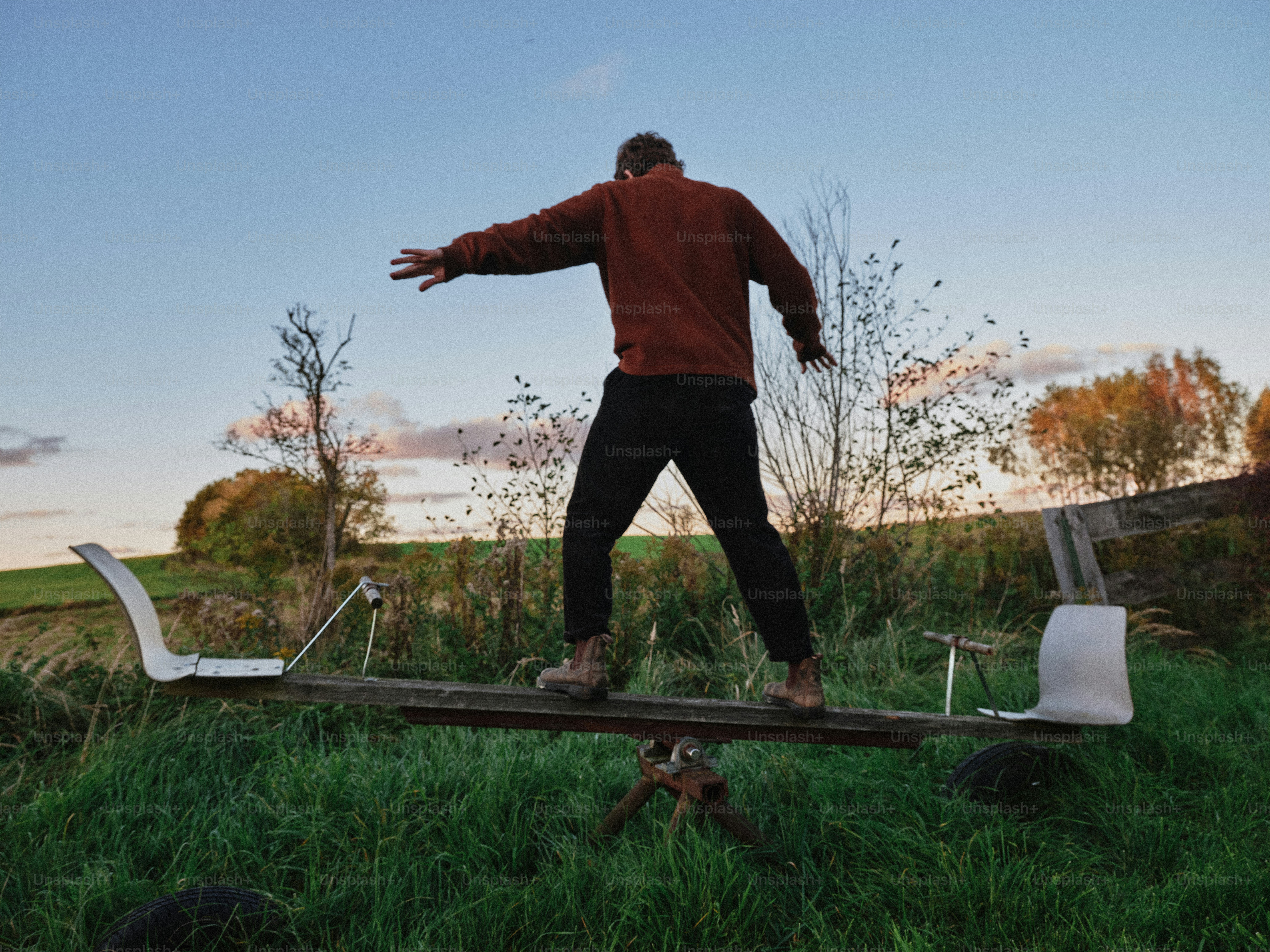 A person in a brown sweater balancing on a seesaw in a grassy field