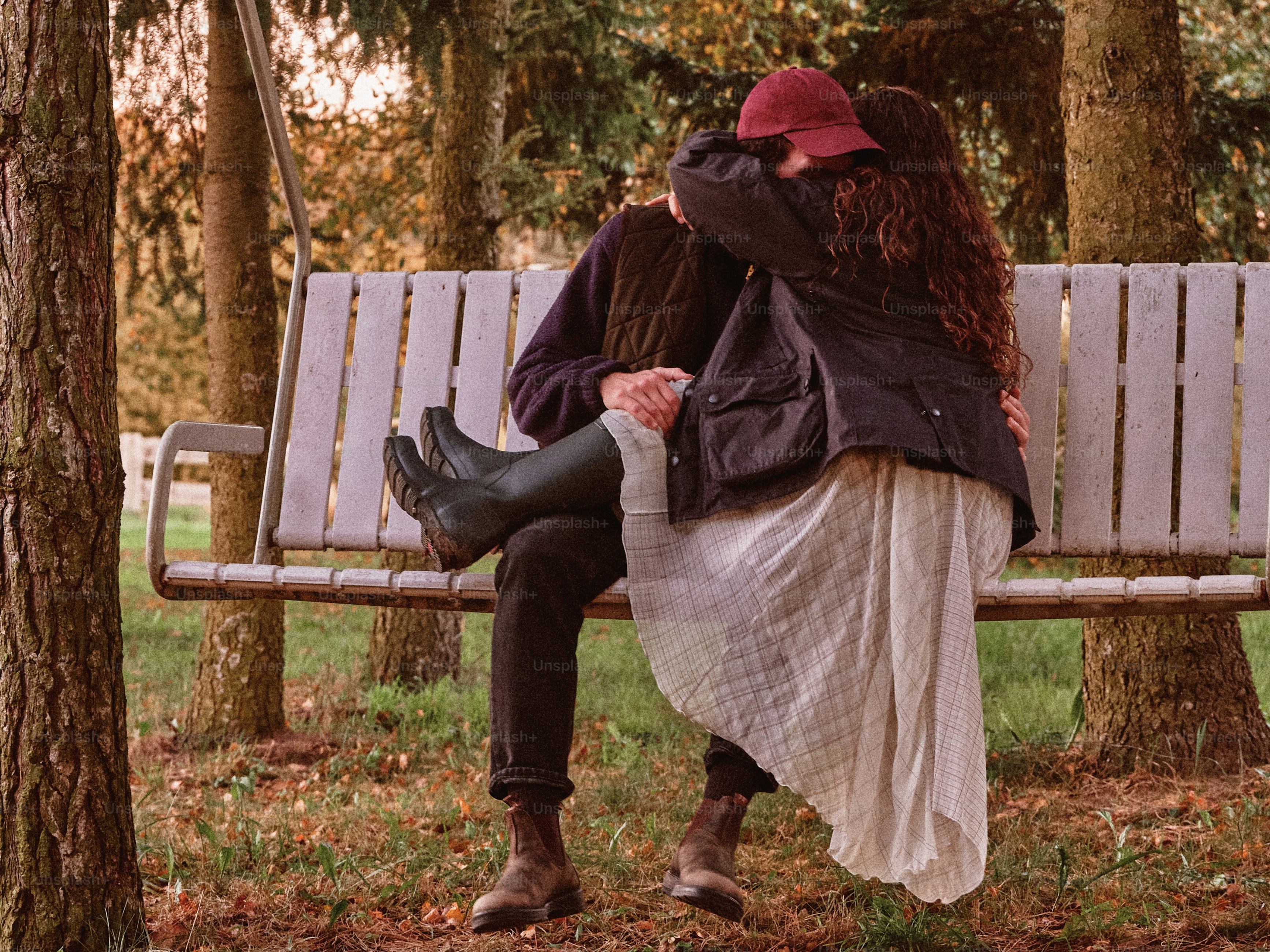 Two people embracing on a hanging bench in a park during autumn