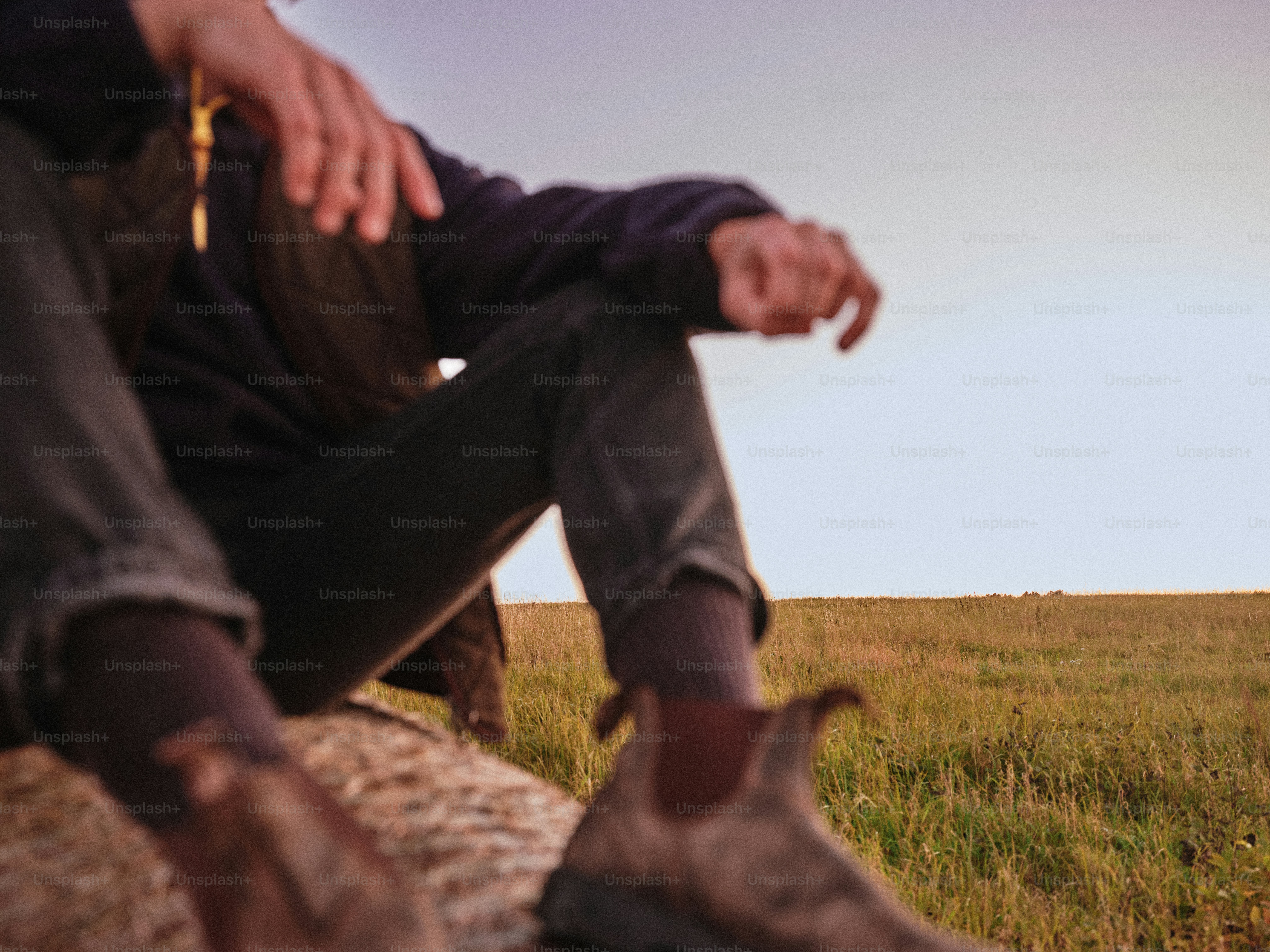 A person in dark clothing and brown boots resting on a grassy field