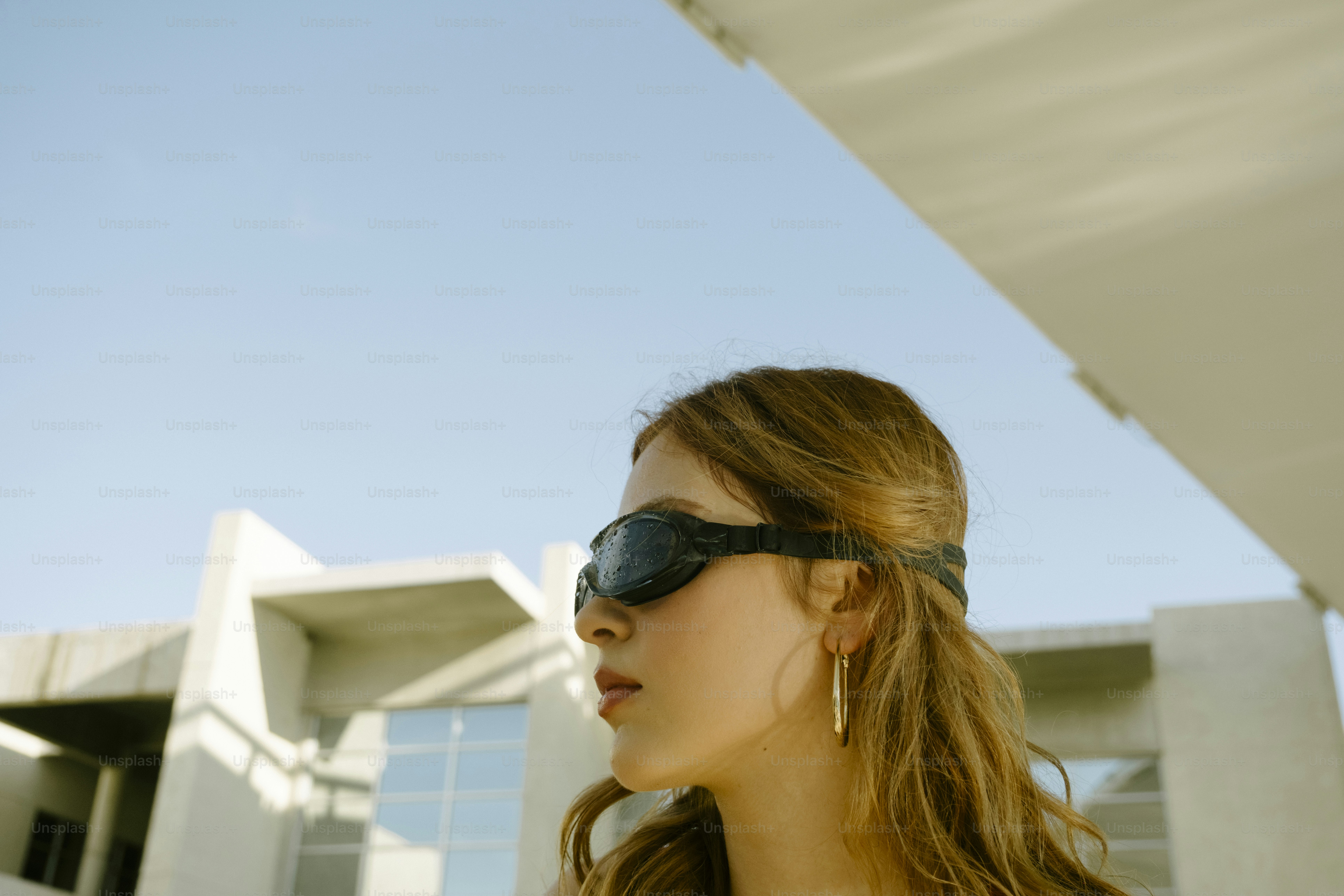 Uma mulher usando óculos de natação pretos contra um céu azul brilhante e um prédio moderno