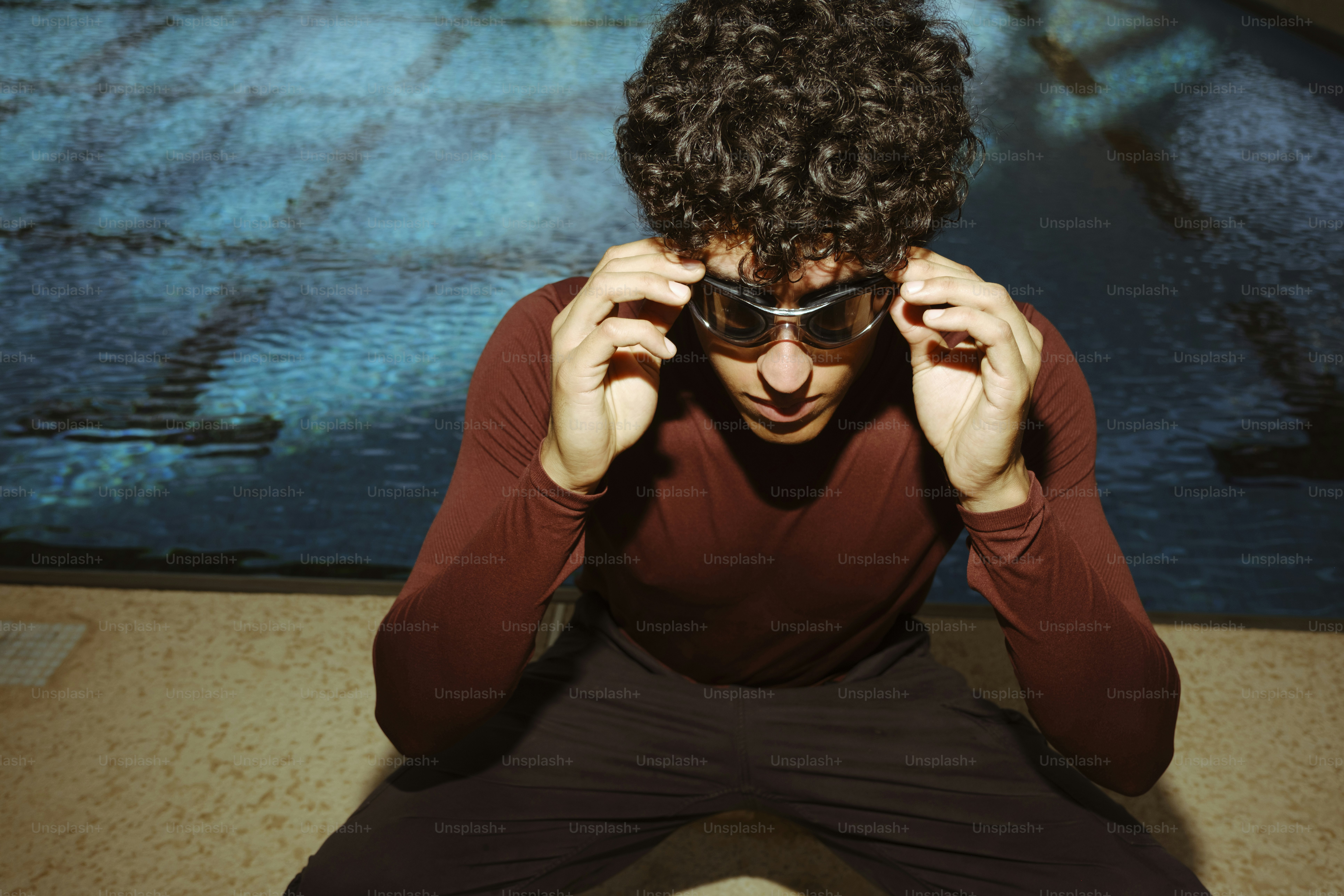A person with curly hair adjusting swimming goggles beside a blue pool
