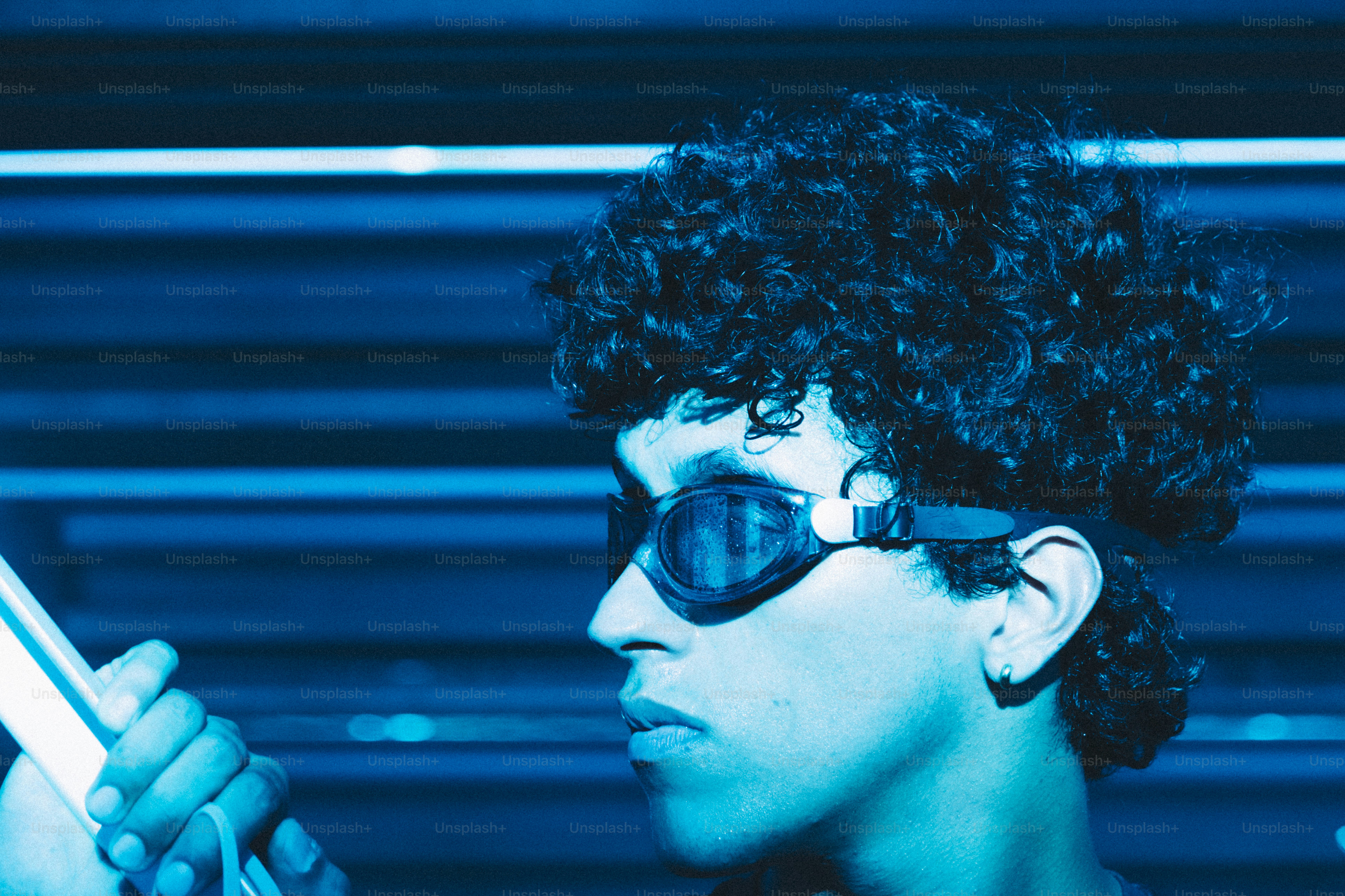 A person with curly hair wearing swimming goggles in bright blue light