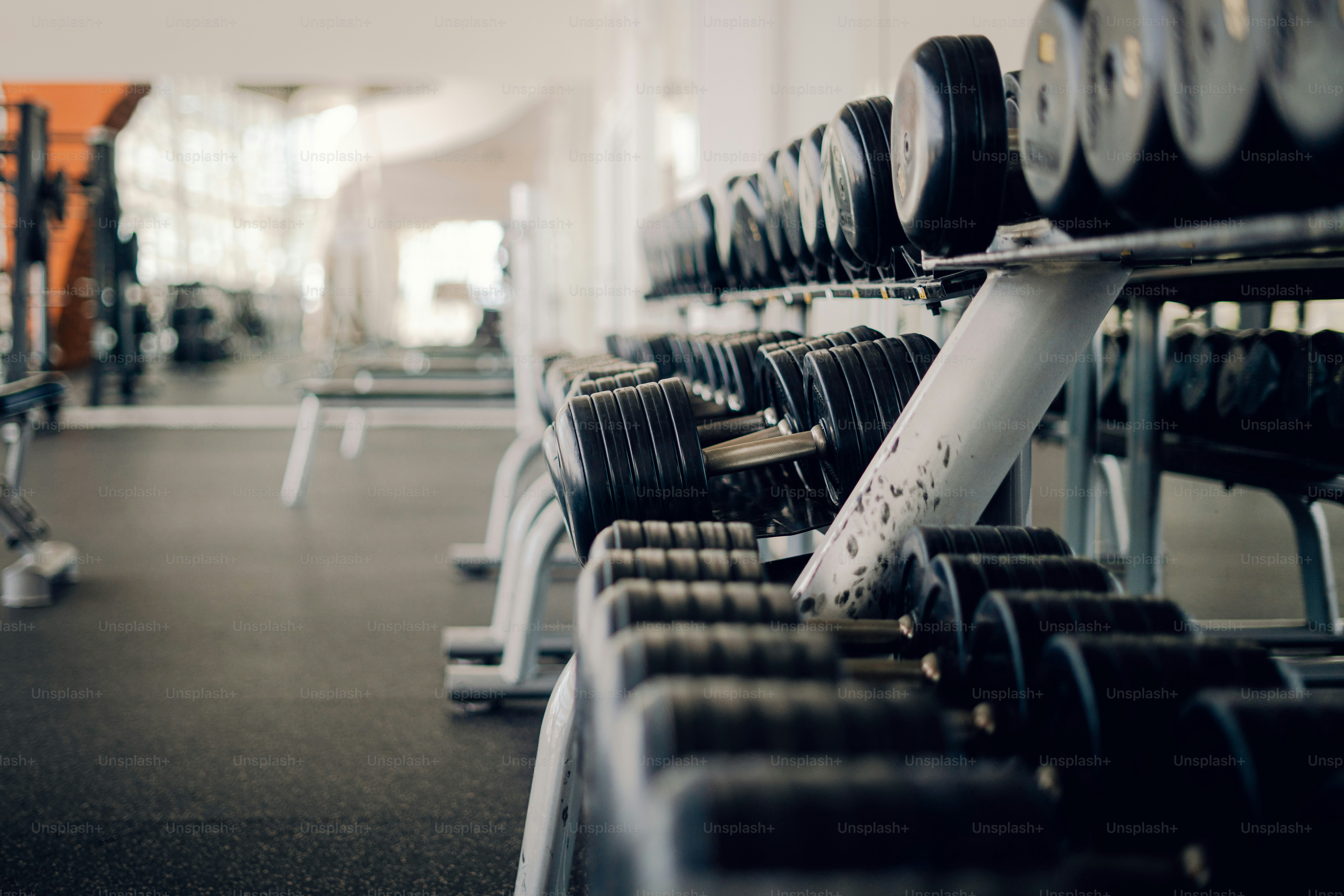 Rows of black dumbbells on a metal rack in a gym