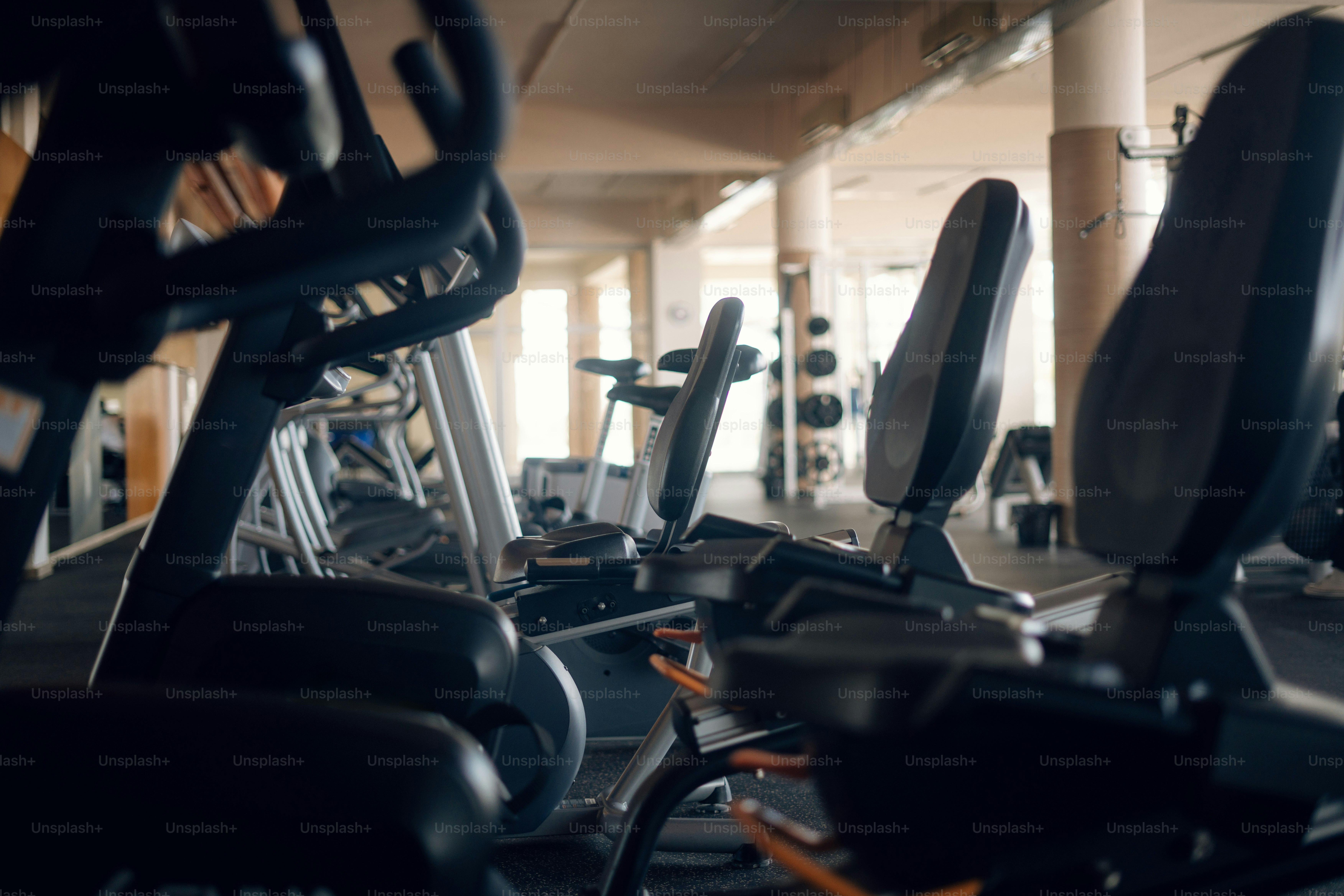Stationary exercise bikes lined up in a row inside a bright gym