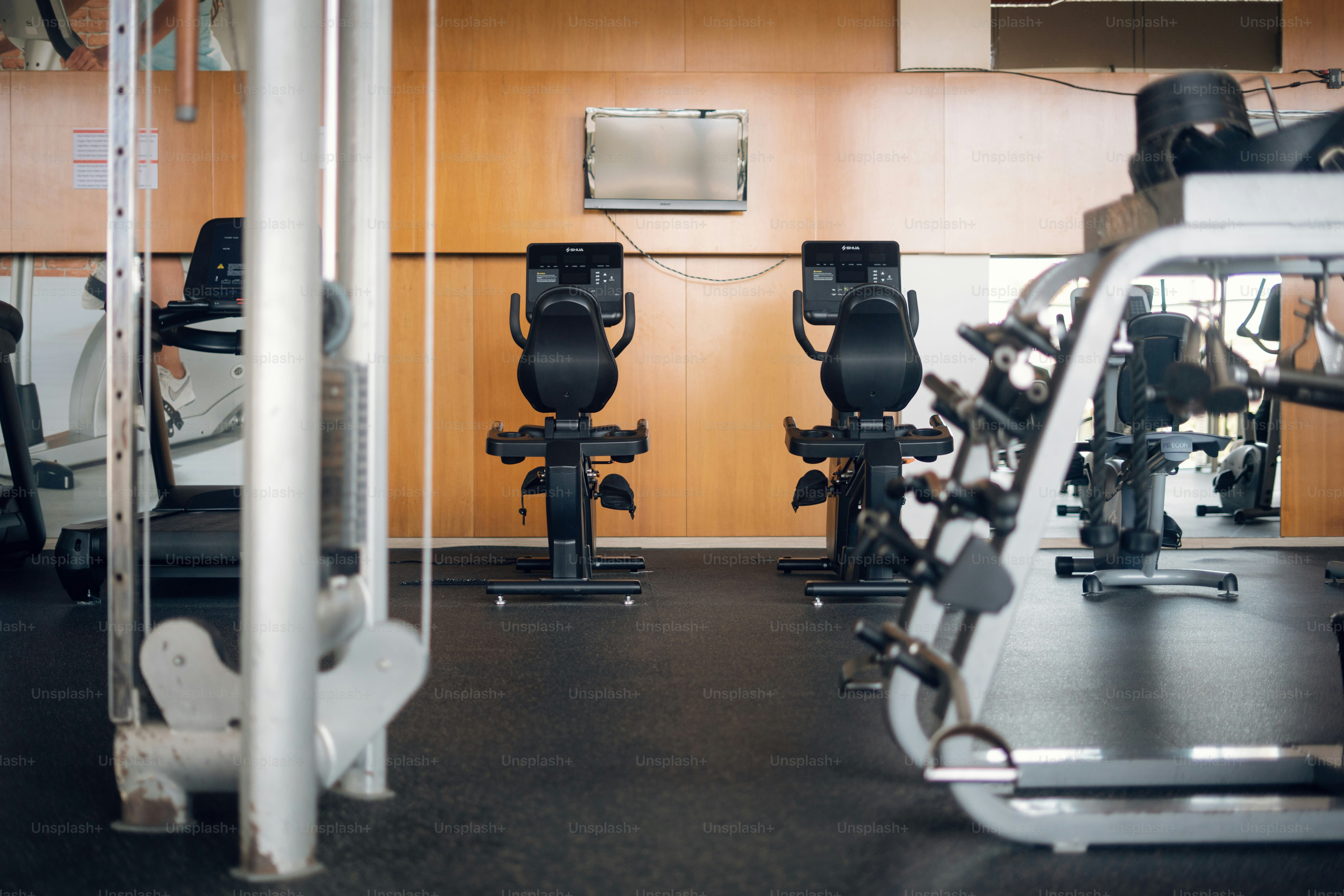Two stationary exercise bikes in a gym with wood paneled walls