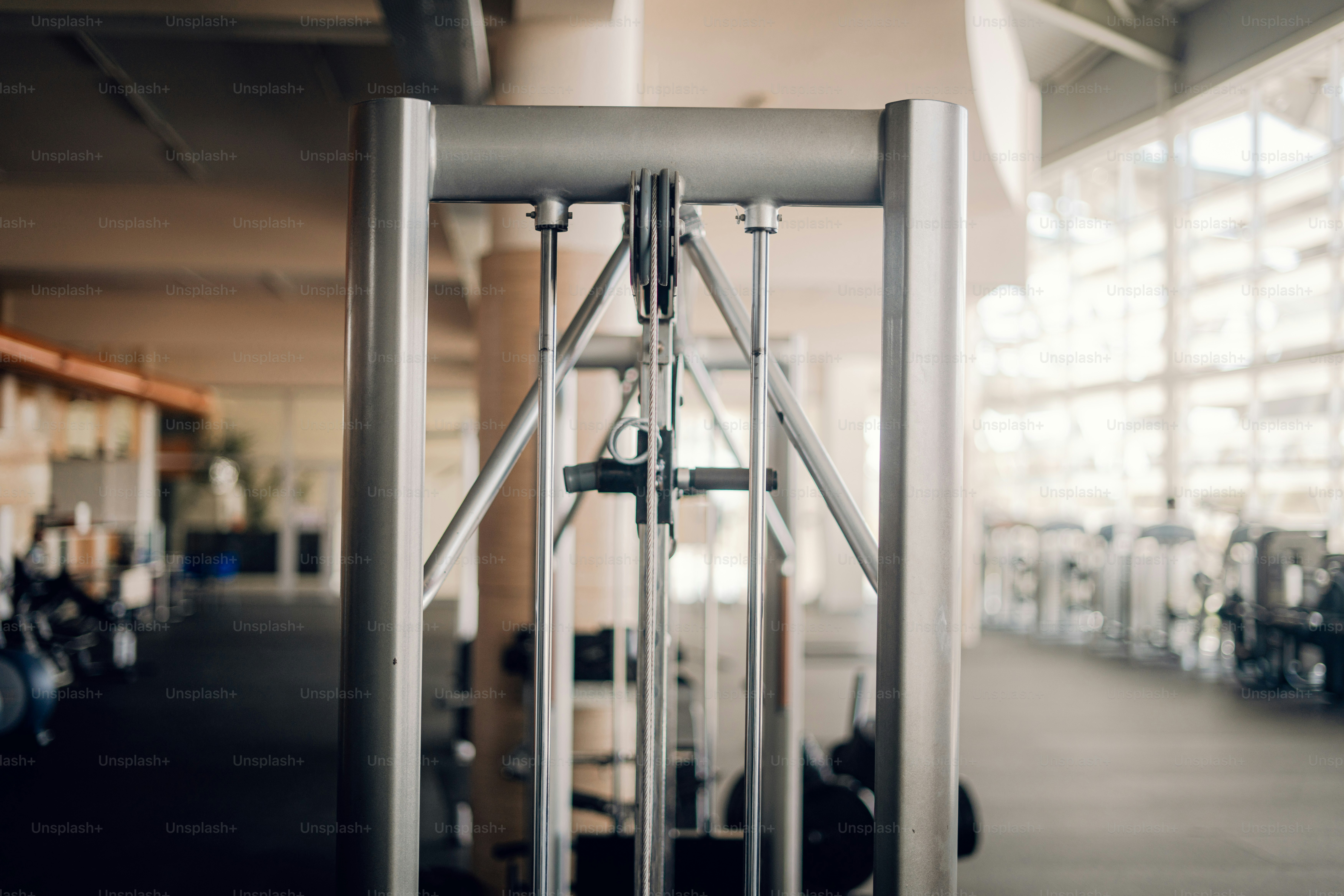 A silver cable machine in a bright gym with large windows