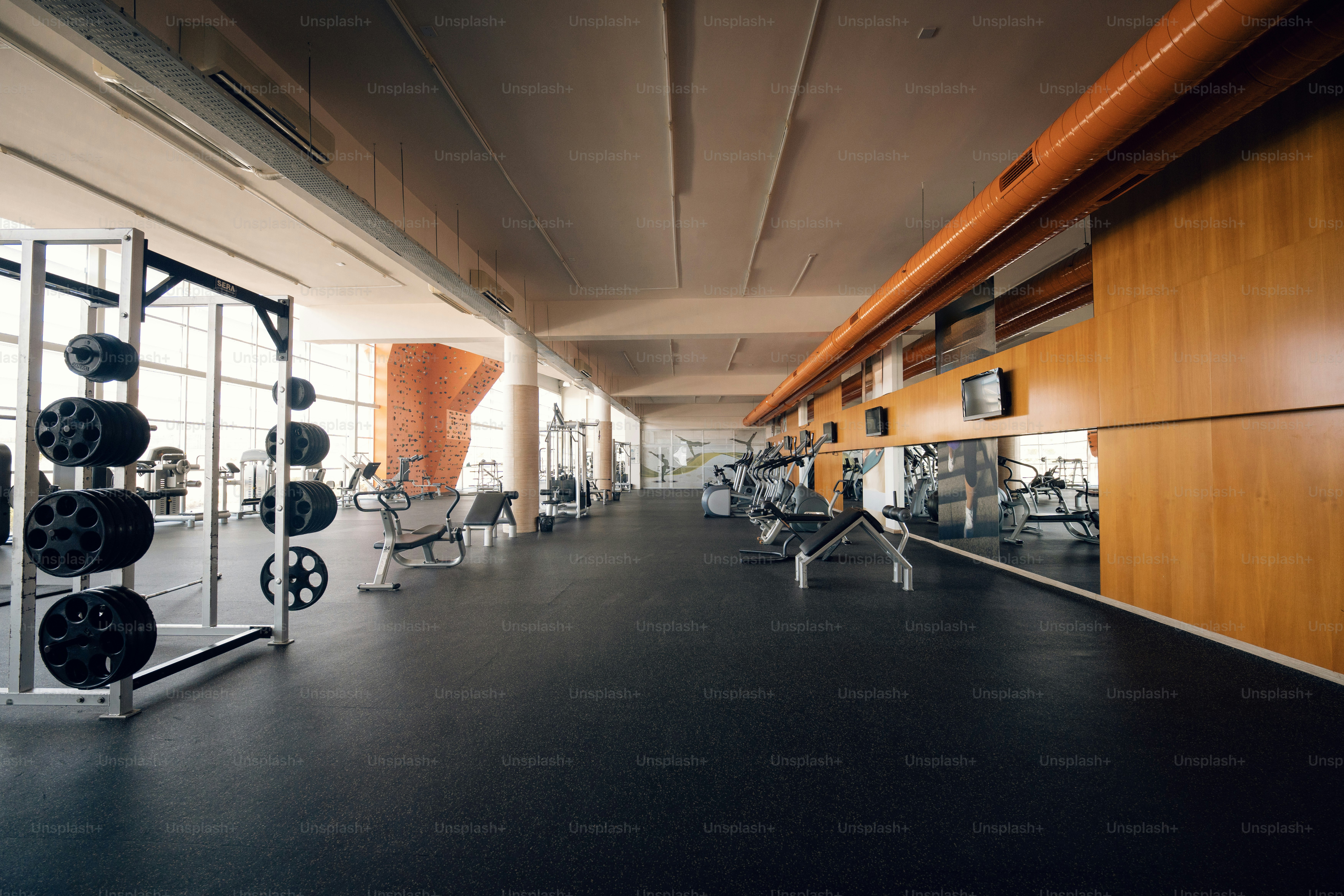A spacious gym with weight racks, exercise machines, and an orange climbing wall