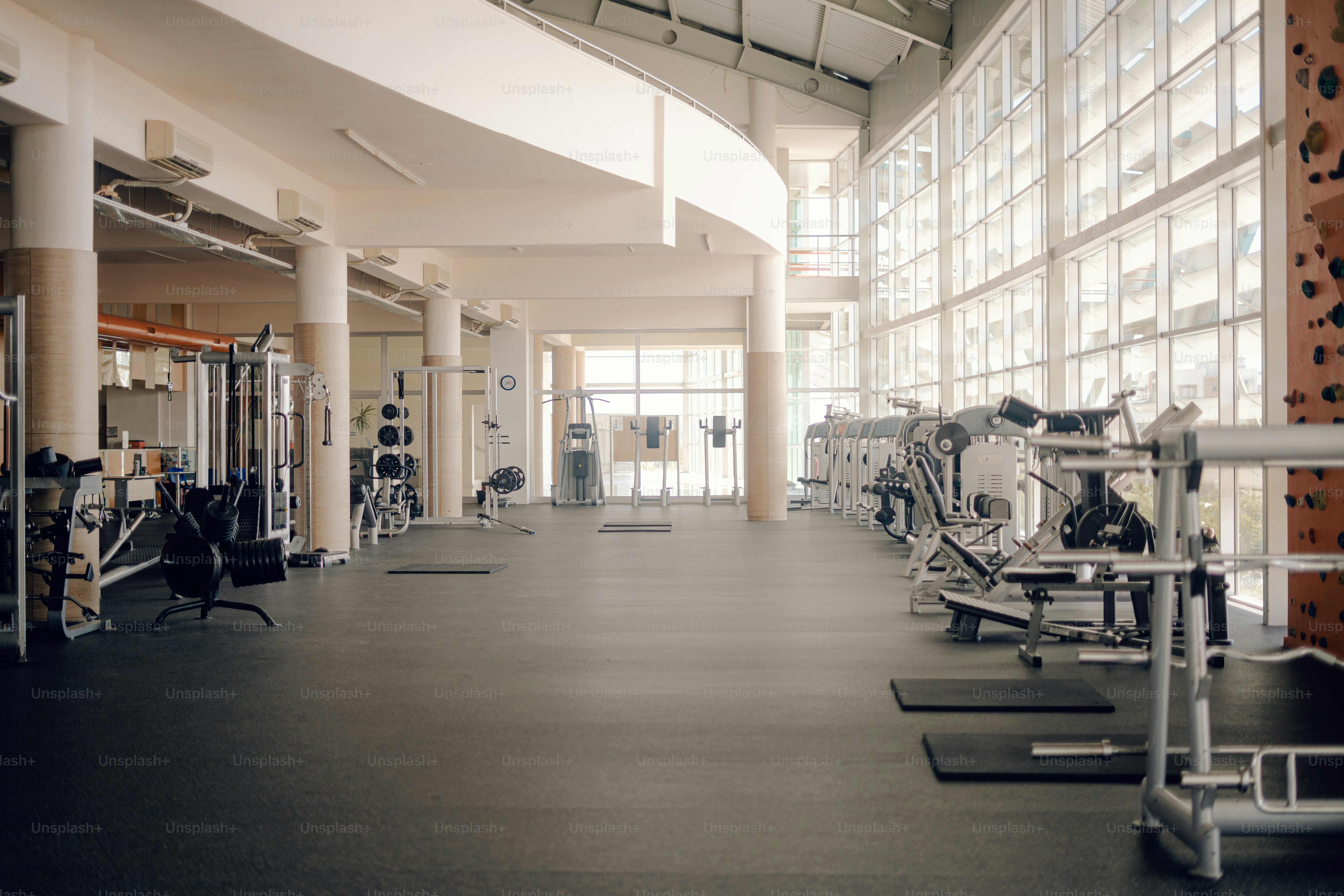 Rows of weight machines and exercise equipment in a sunlit gym with large windows