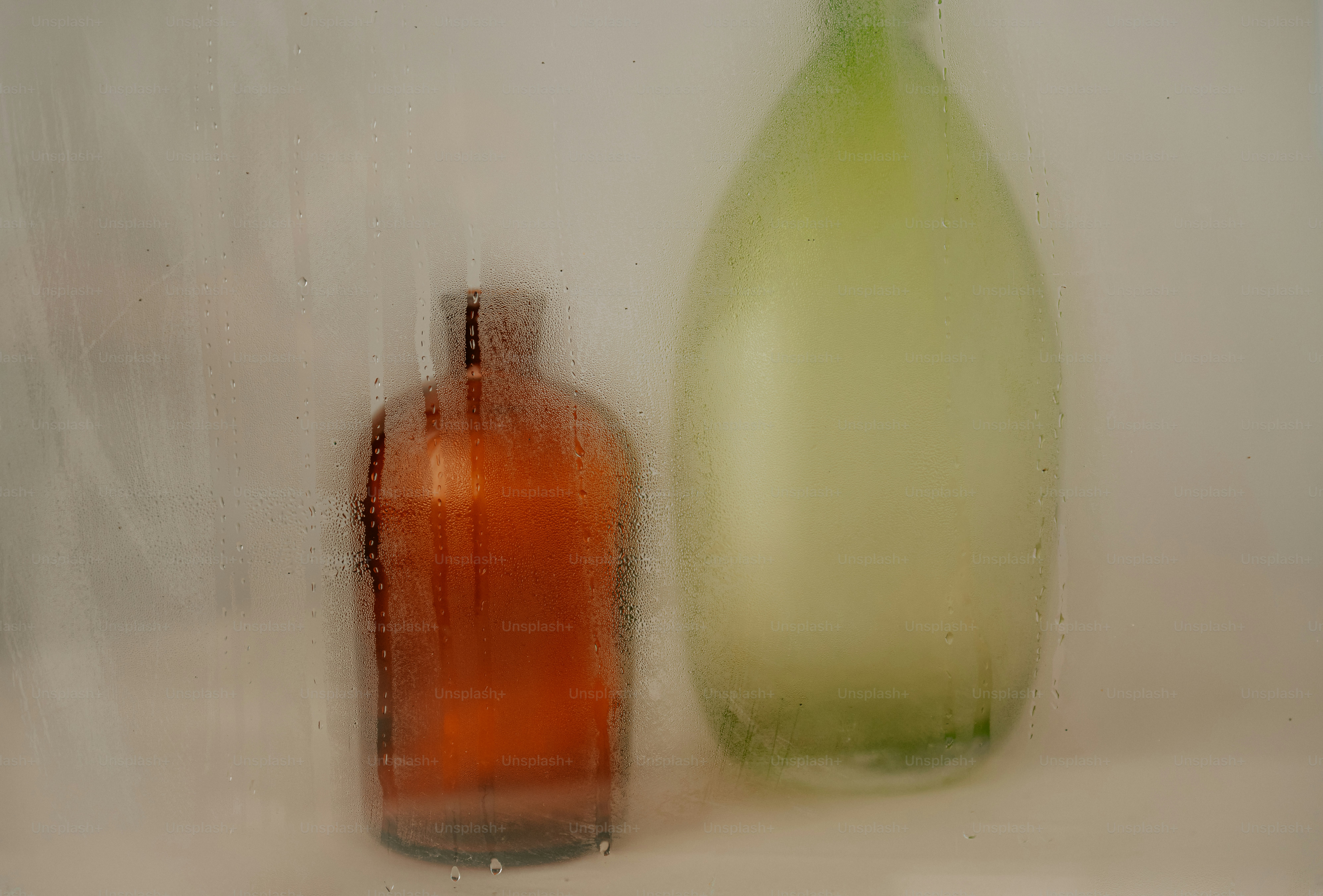 An amber glass bottle and a green glass bottle behind a steamed window