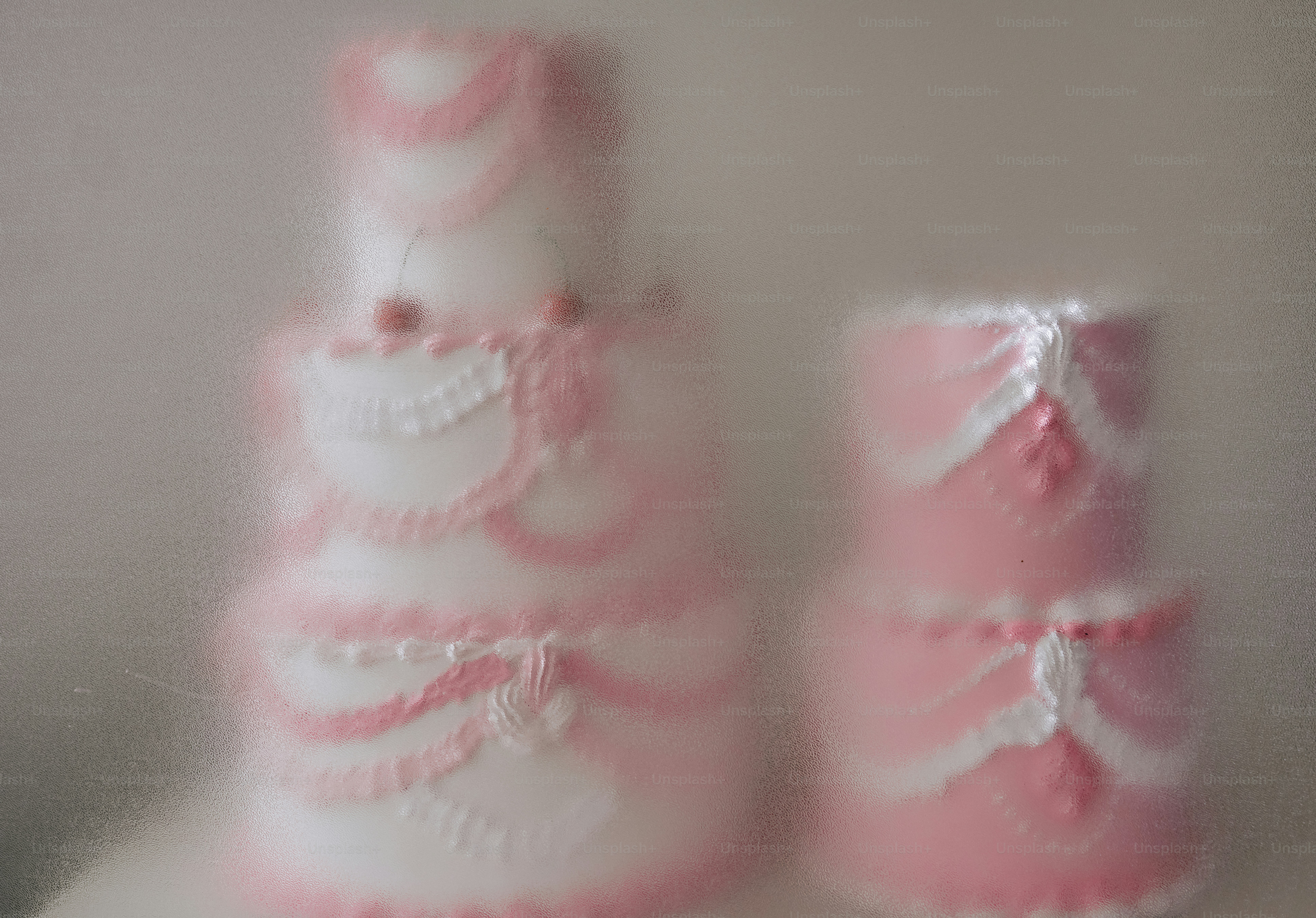 Two blurred cakes with pink and white frosting seen through frosted glass