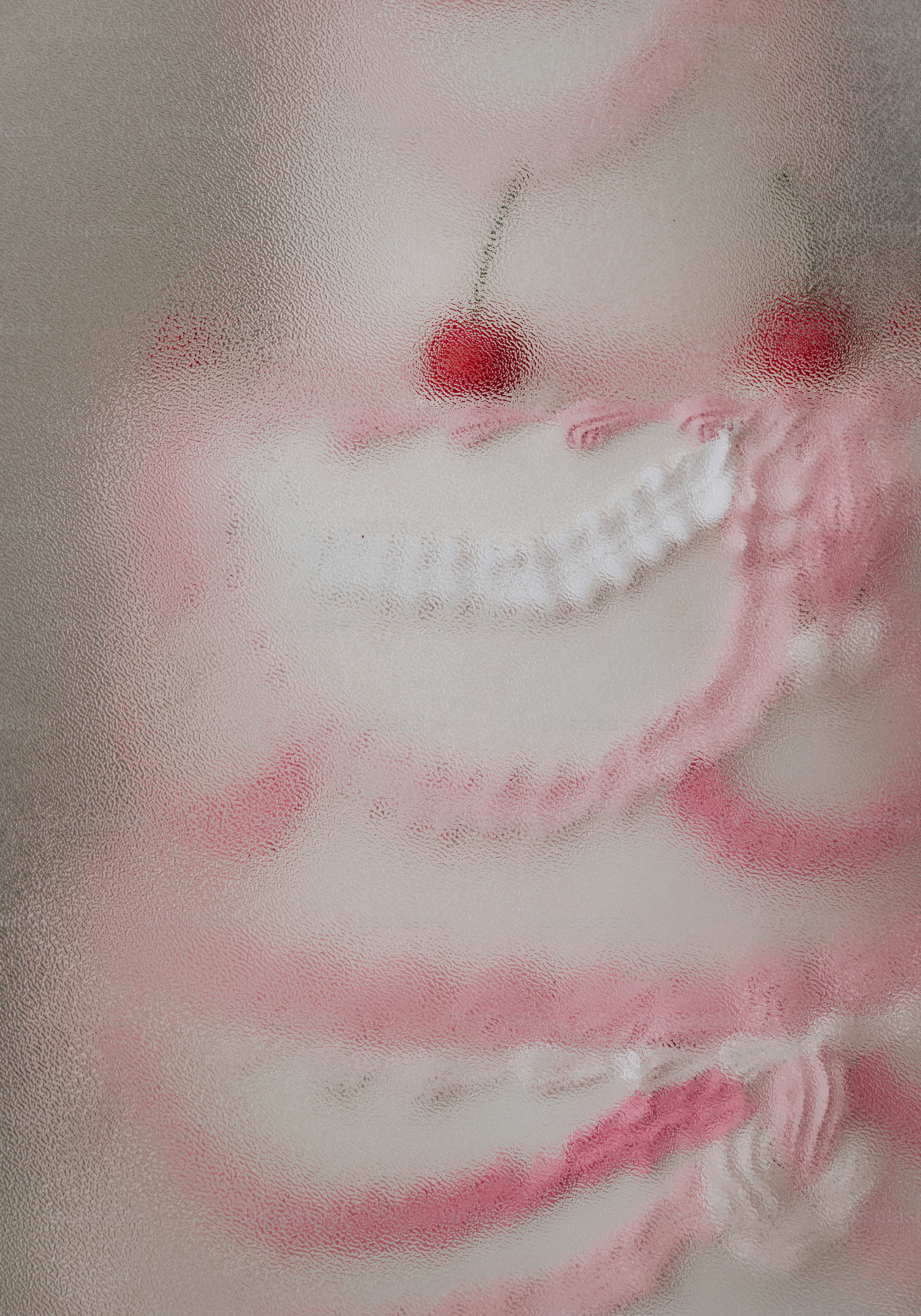A pink and white frosted cake with cherries behind textured glass