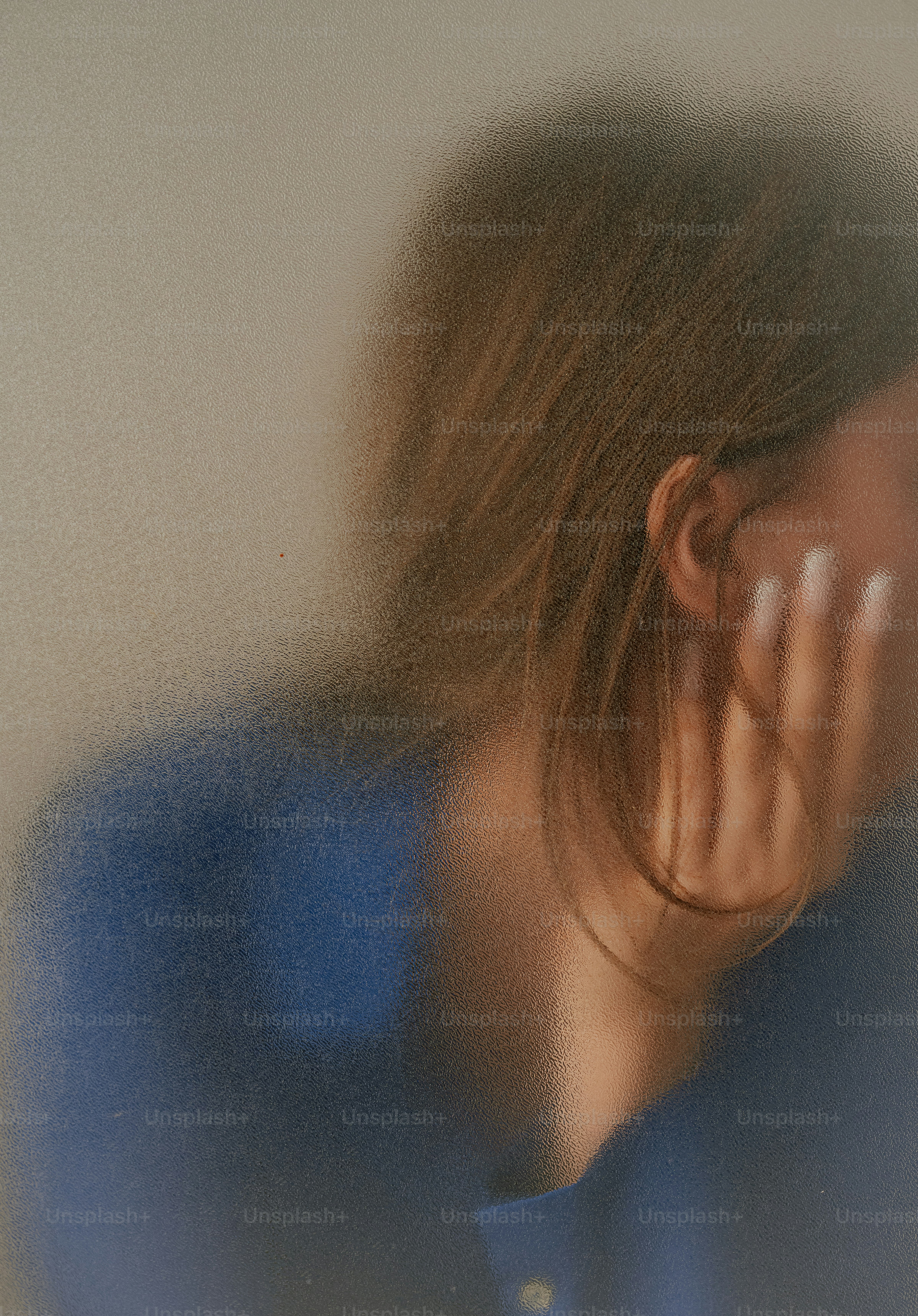 A person with brown hair seen through textured frosted glass
