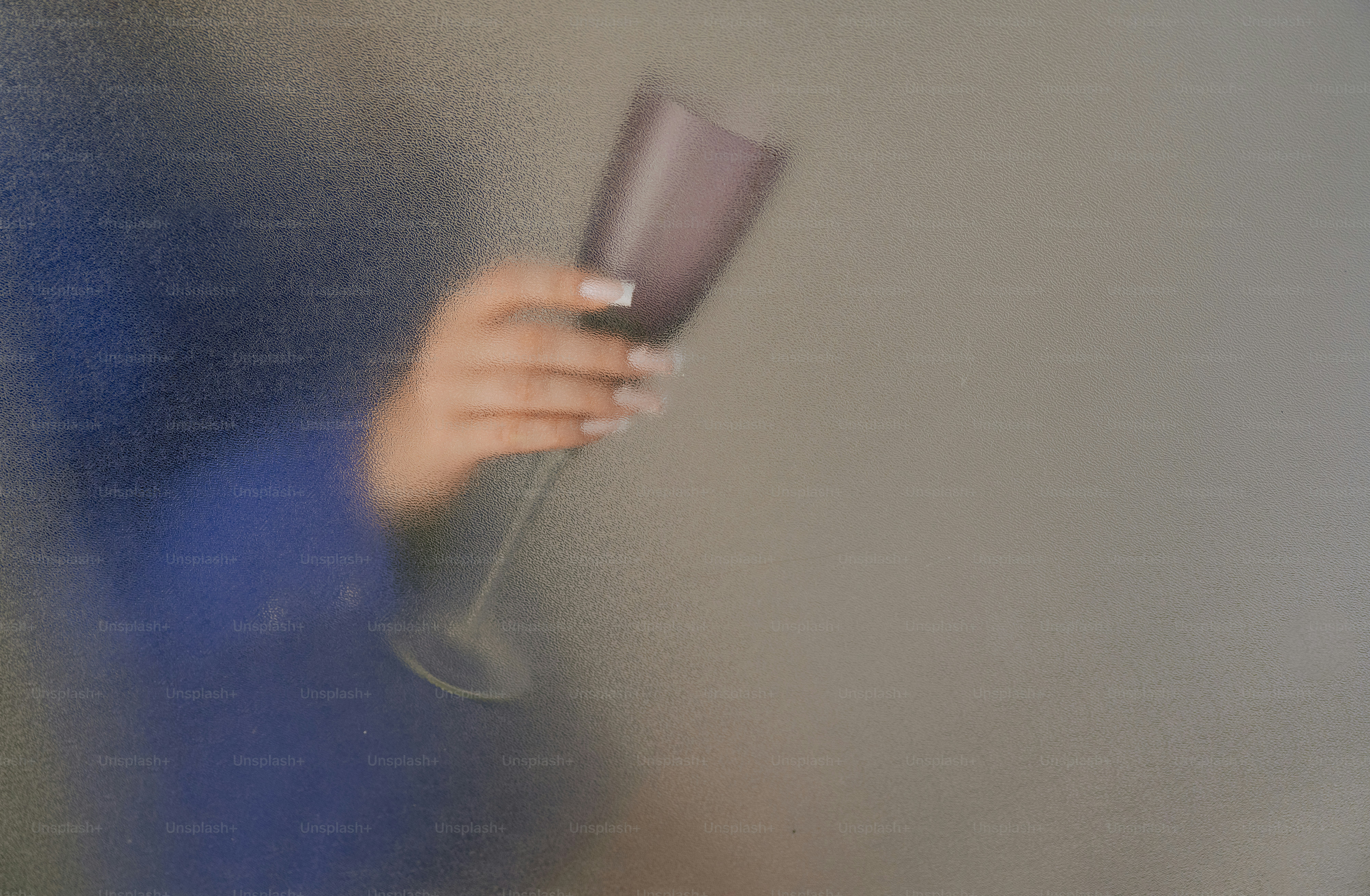 A hand holding a wine glass behind a textured frosted glass surface