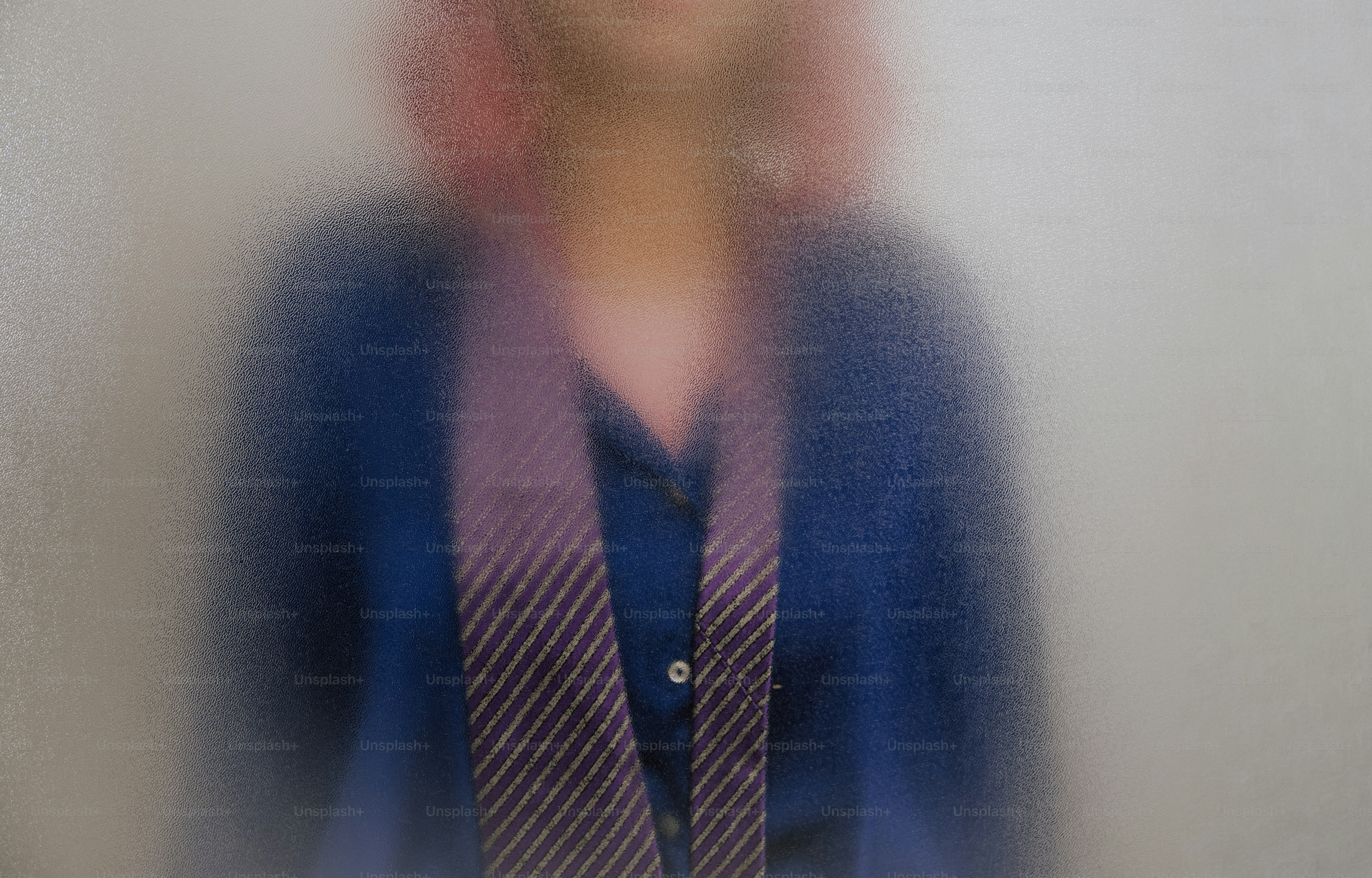 A person in a blue shirt and striped tie behind frosted glass