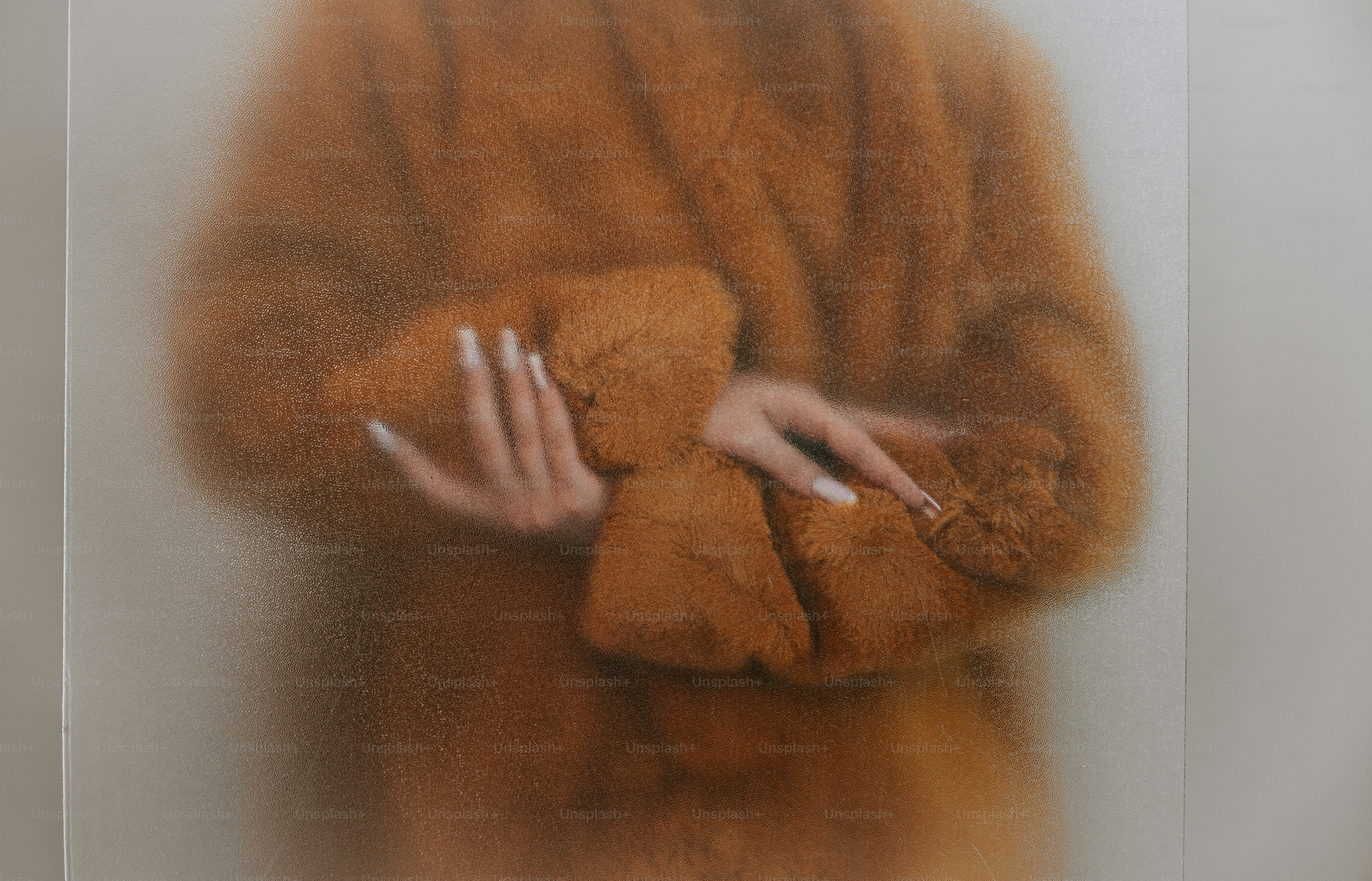 A person in a brown faux fur coat behind frosted glass