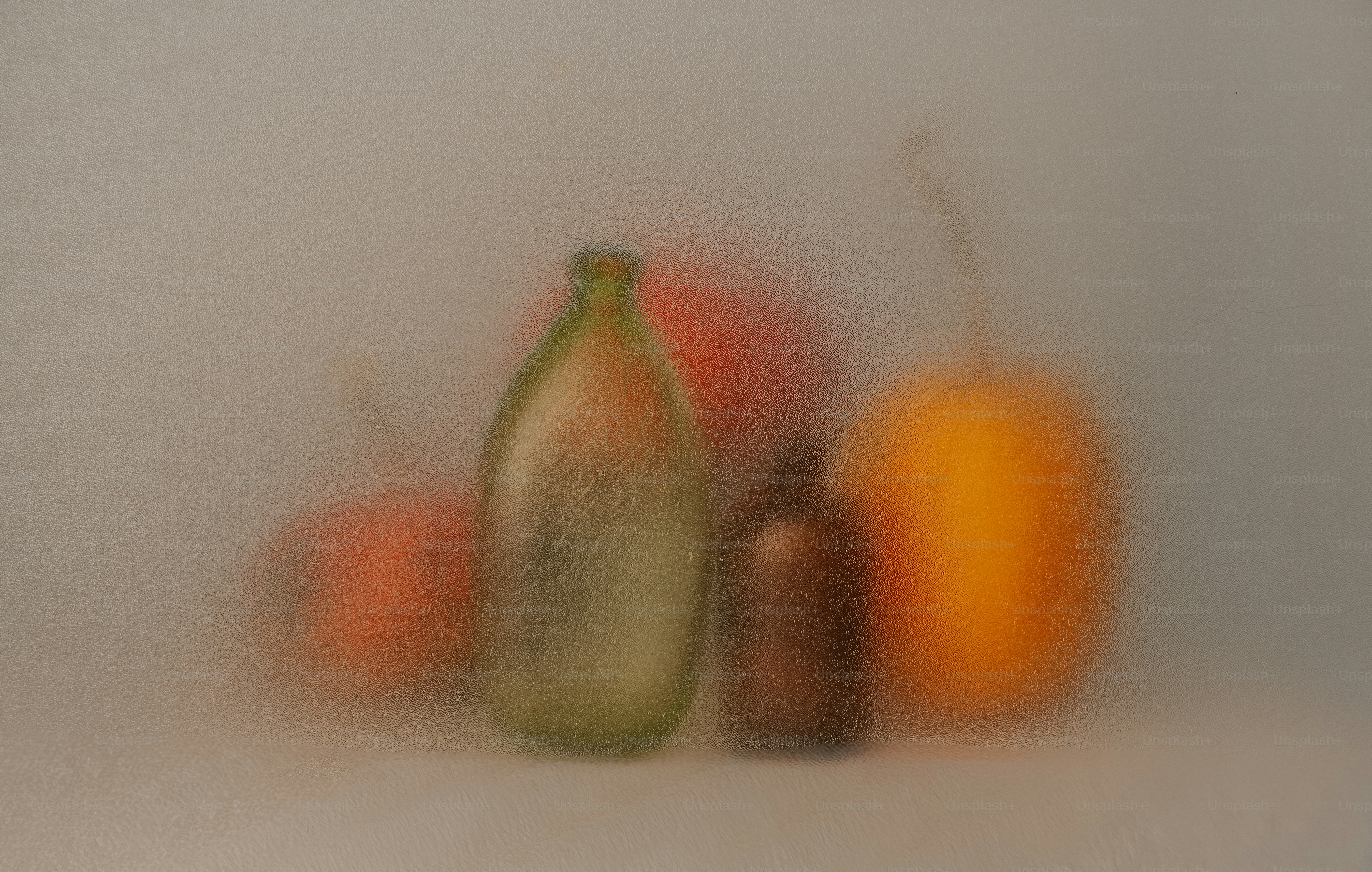 A green bottle and a brown bottle beside fruit behind frosted glass