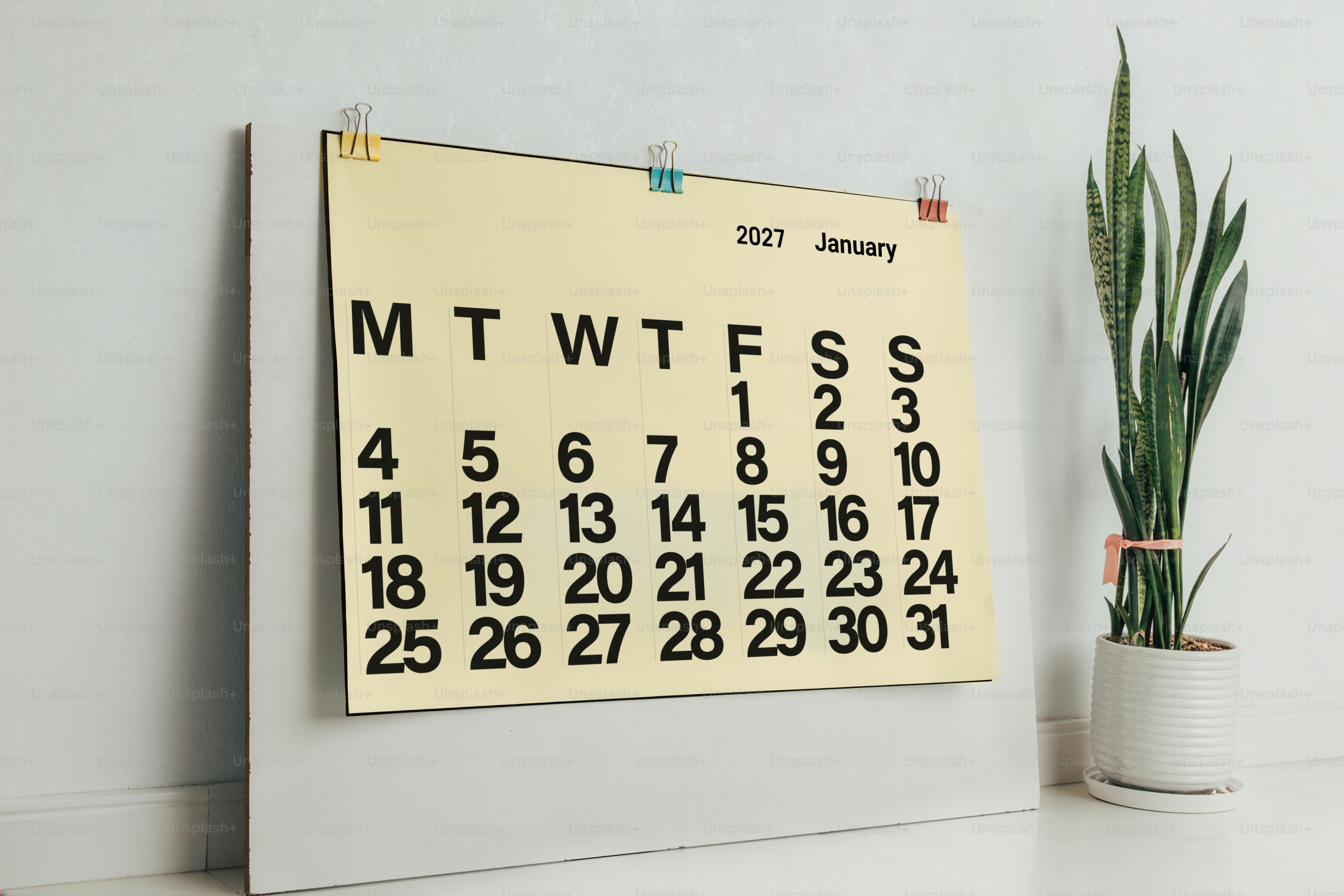 A January 2027 calendar page clipped to a board beside a snake plant