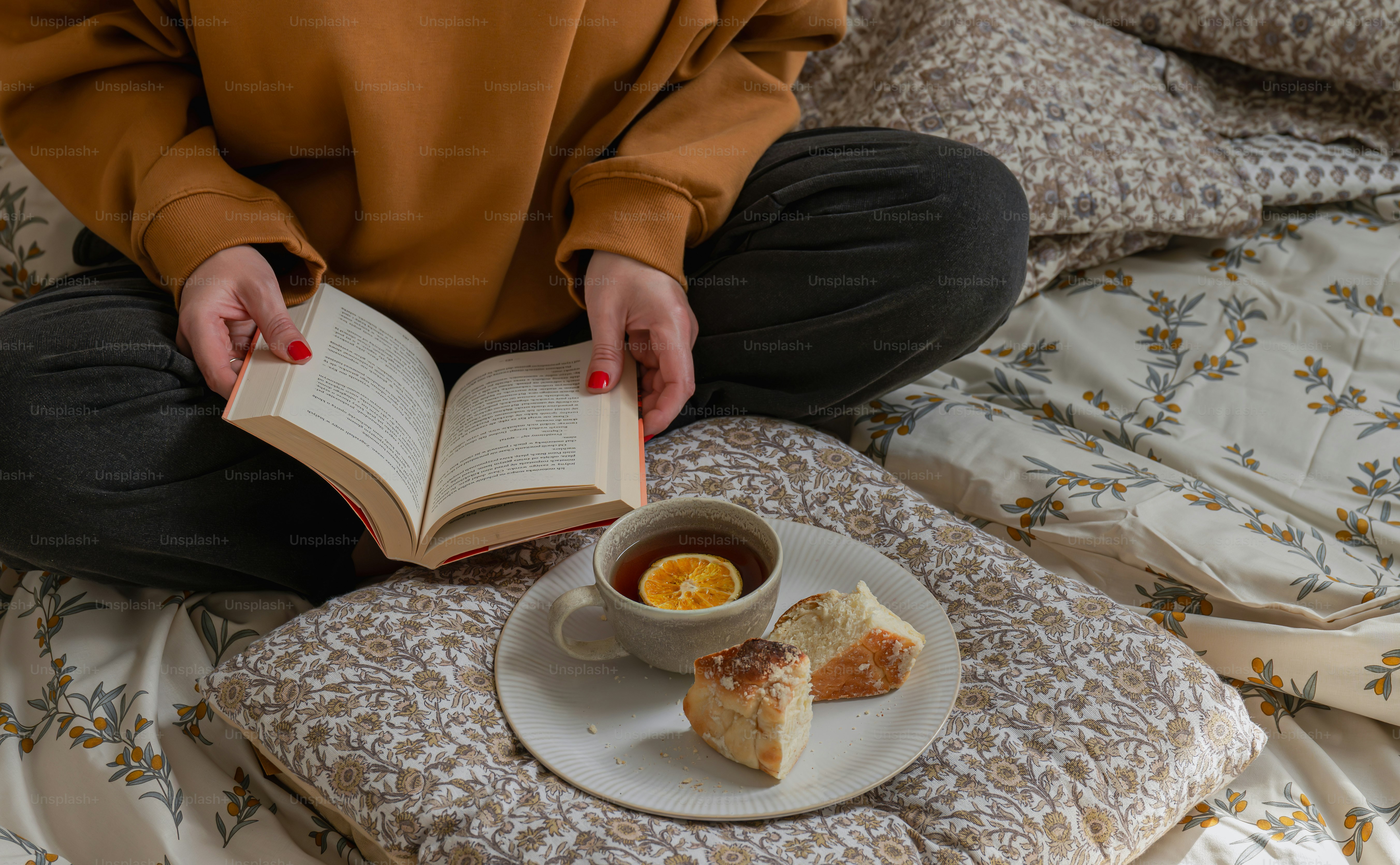 A person in a brown sweatshirt reading a book on a floral bedspread