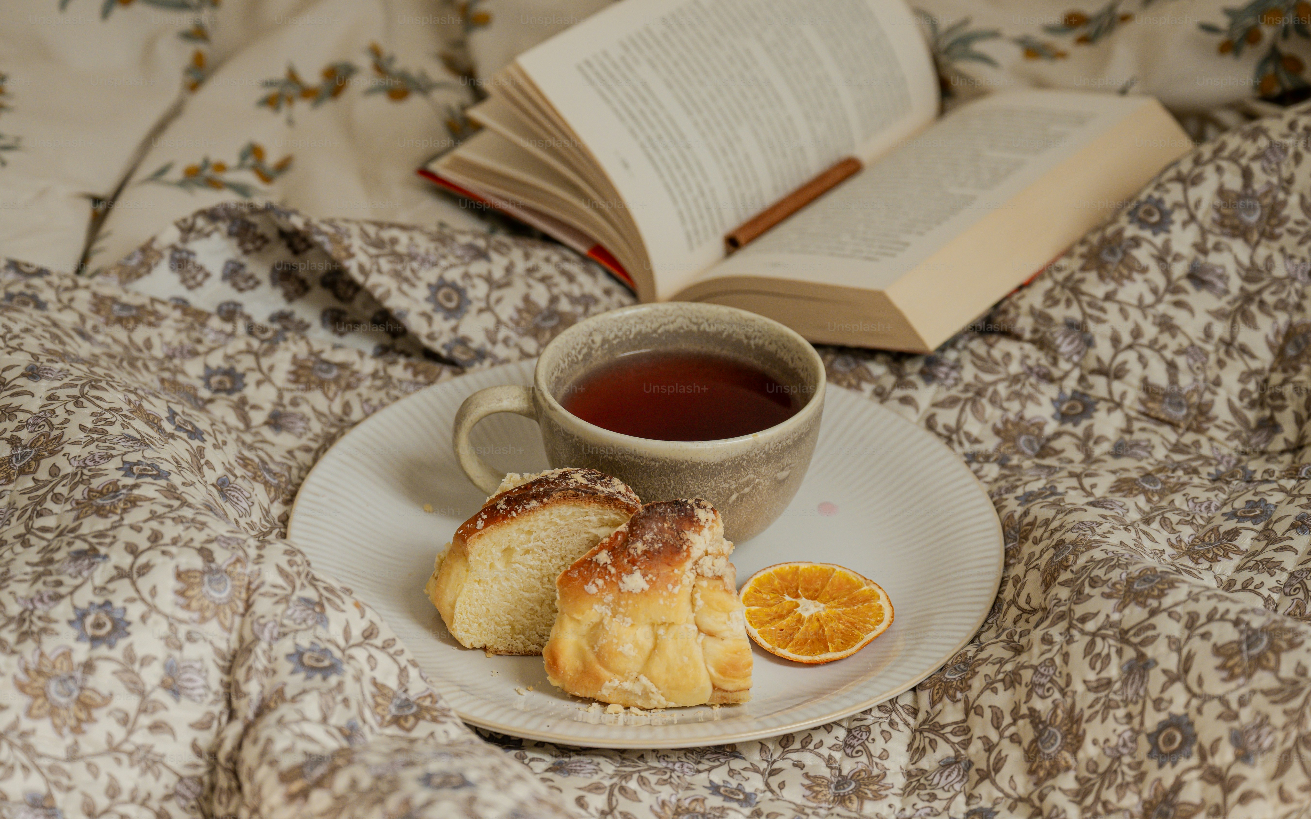 A cup of tea, pastry, and dried orange slice on a plate with a book