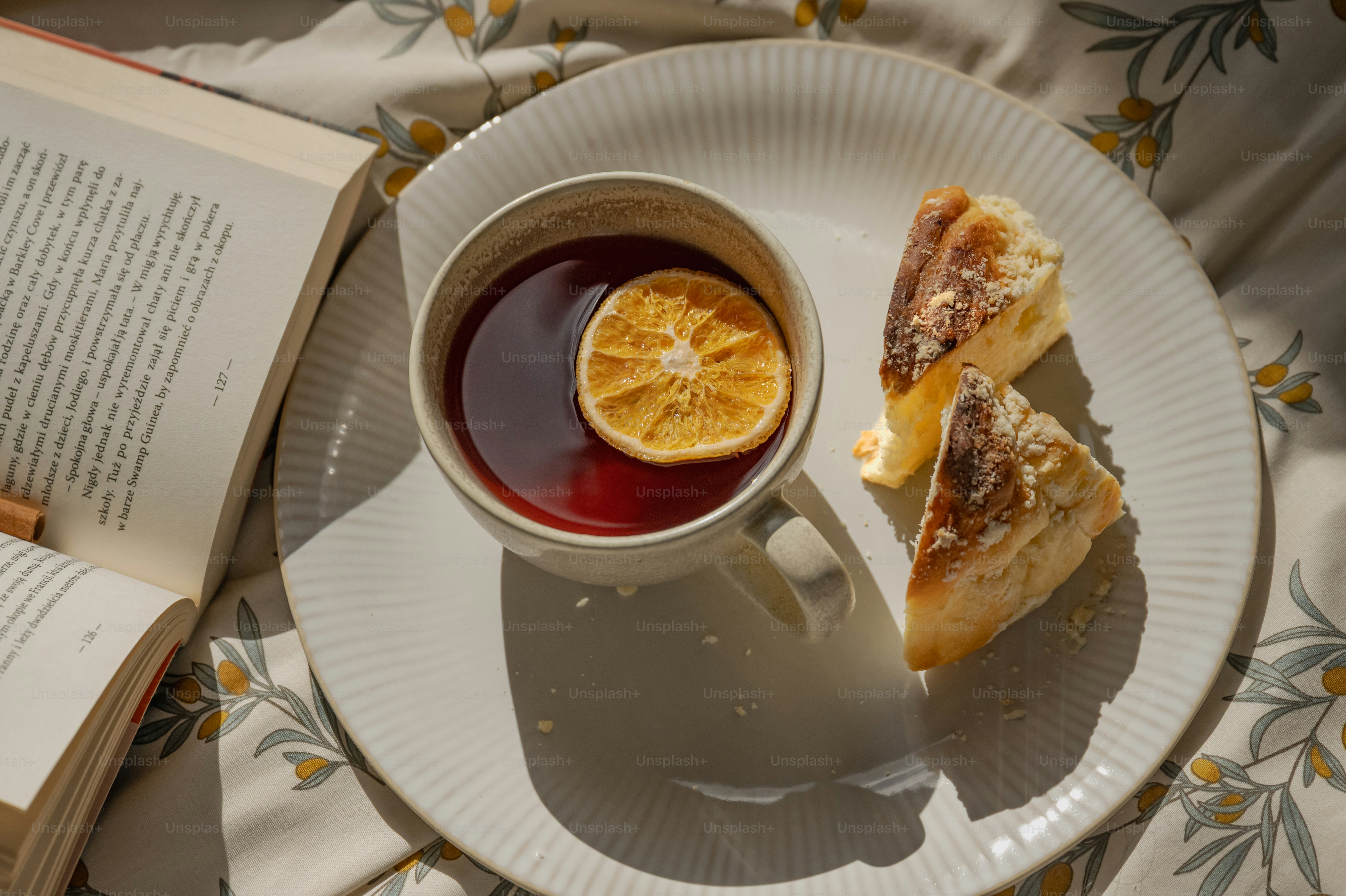 A cup of tea with a dried orange slice beside cake on a plate