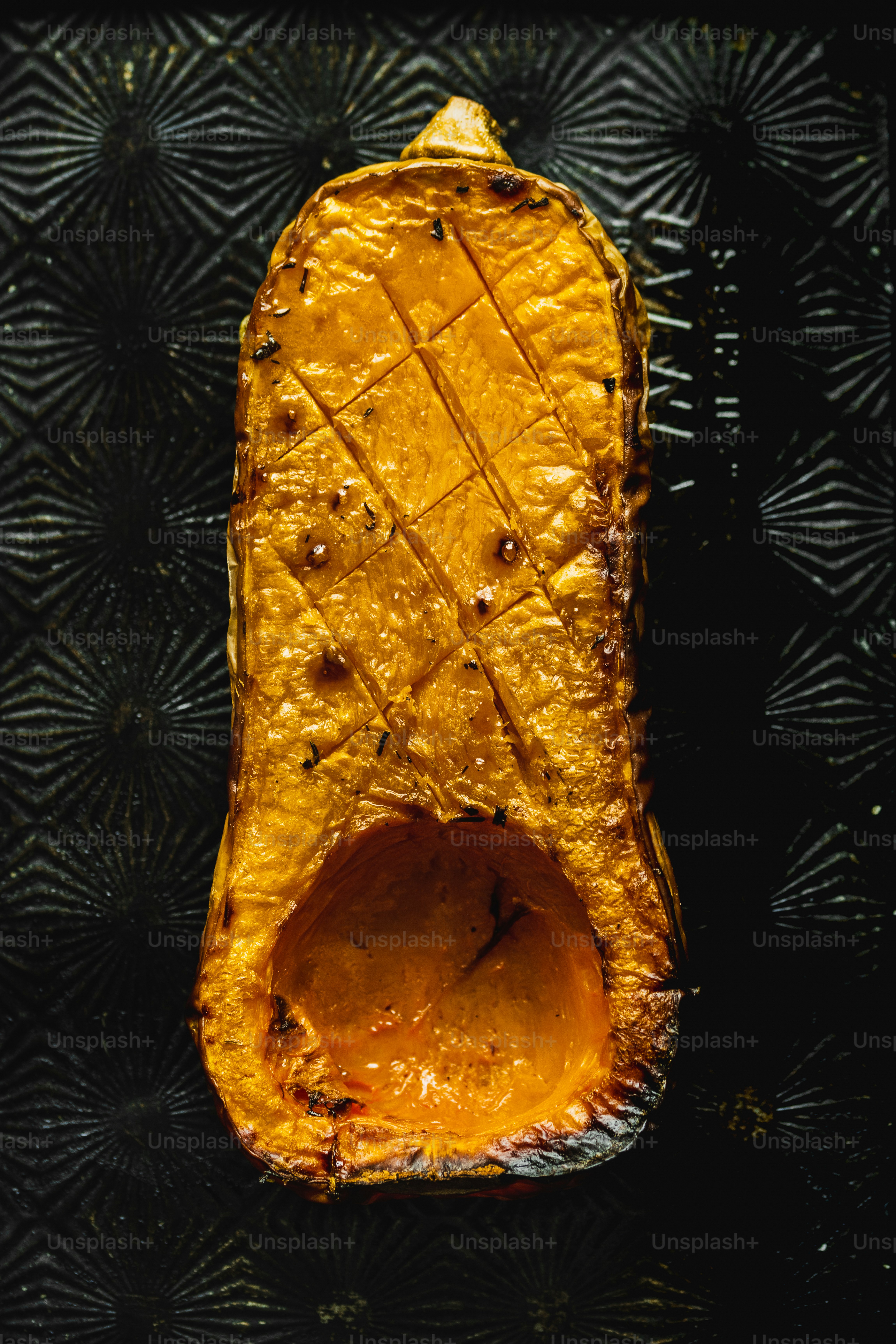 Une moitié de courge musquée rôtie avec un motif de hachures croisées sur un plateau sombre