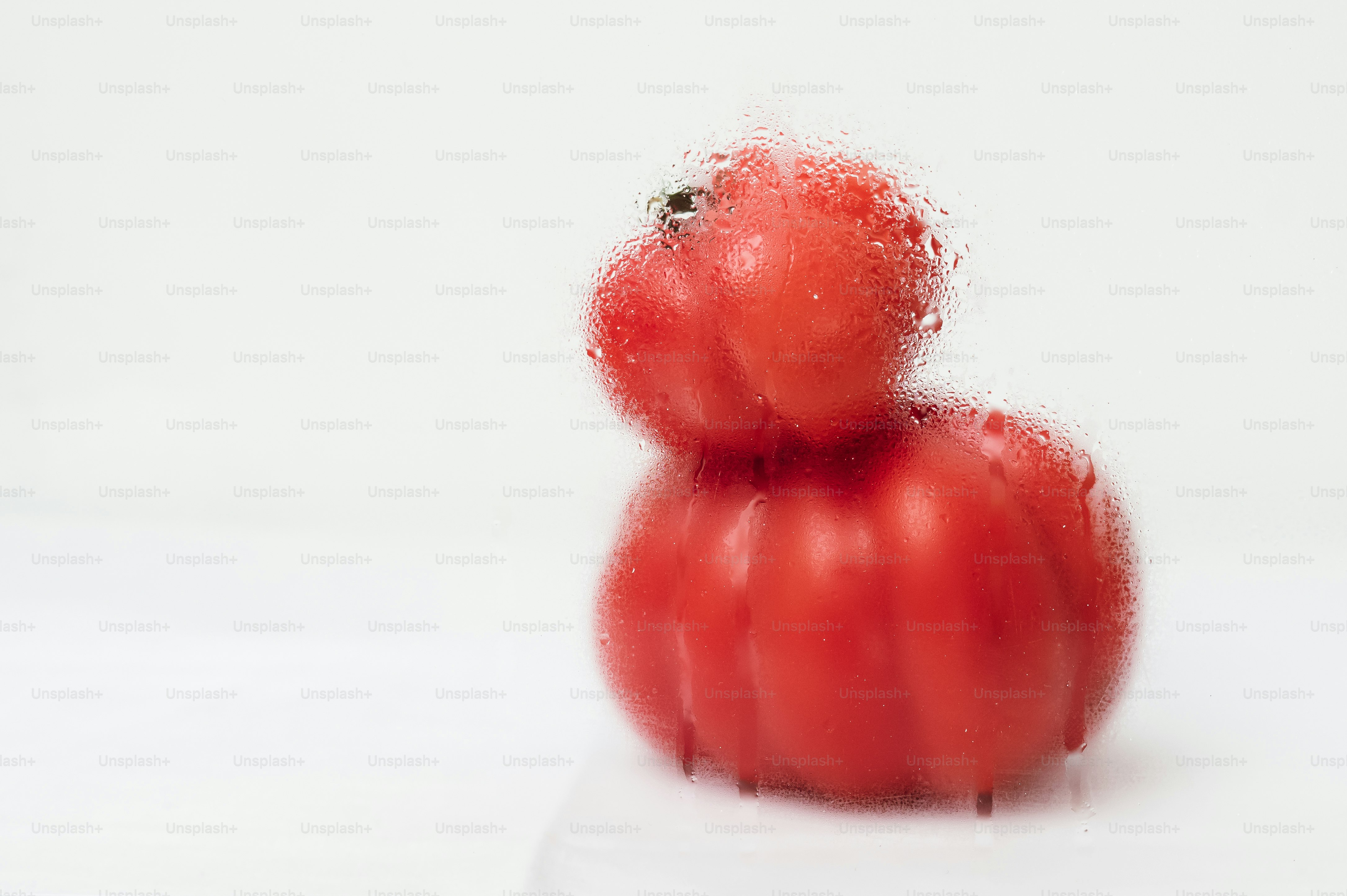 Two stacked red tomatoes behind a glass pane covered in water droplets