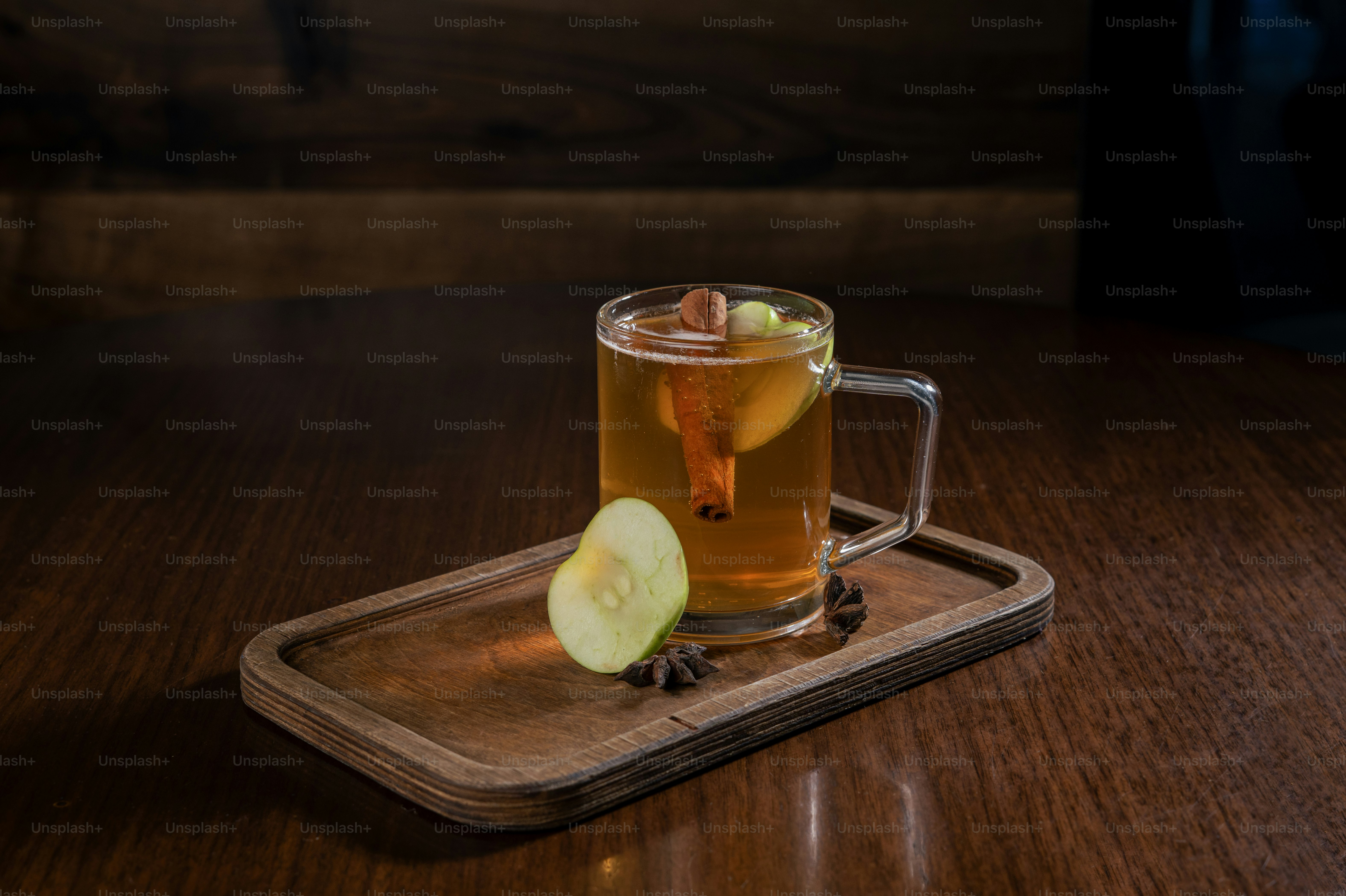 A glass mug of amber tea with a cinnamon stick and apple slice