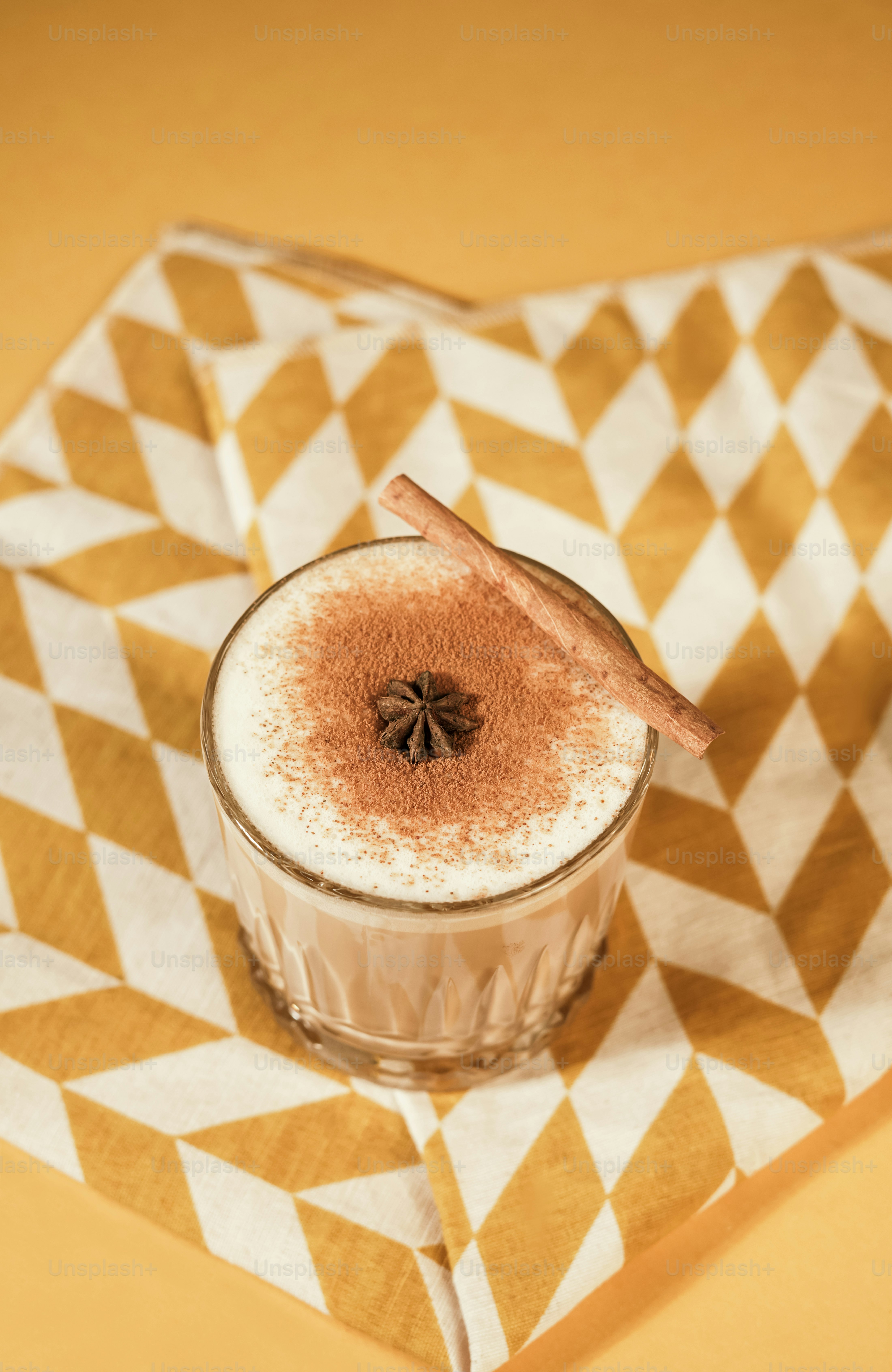 A glass of spiced latte with foam, star anise, and cinnamon on a patterned napkin