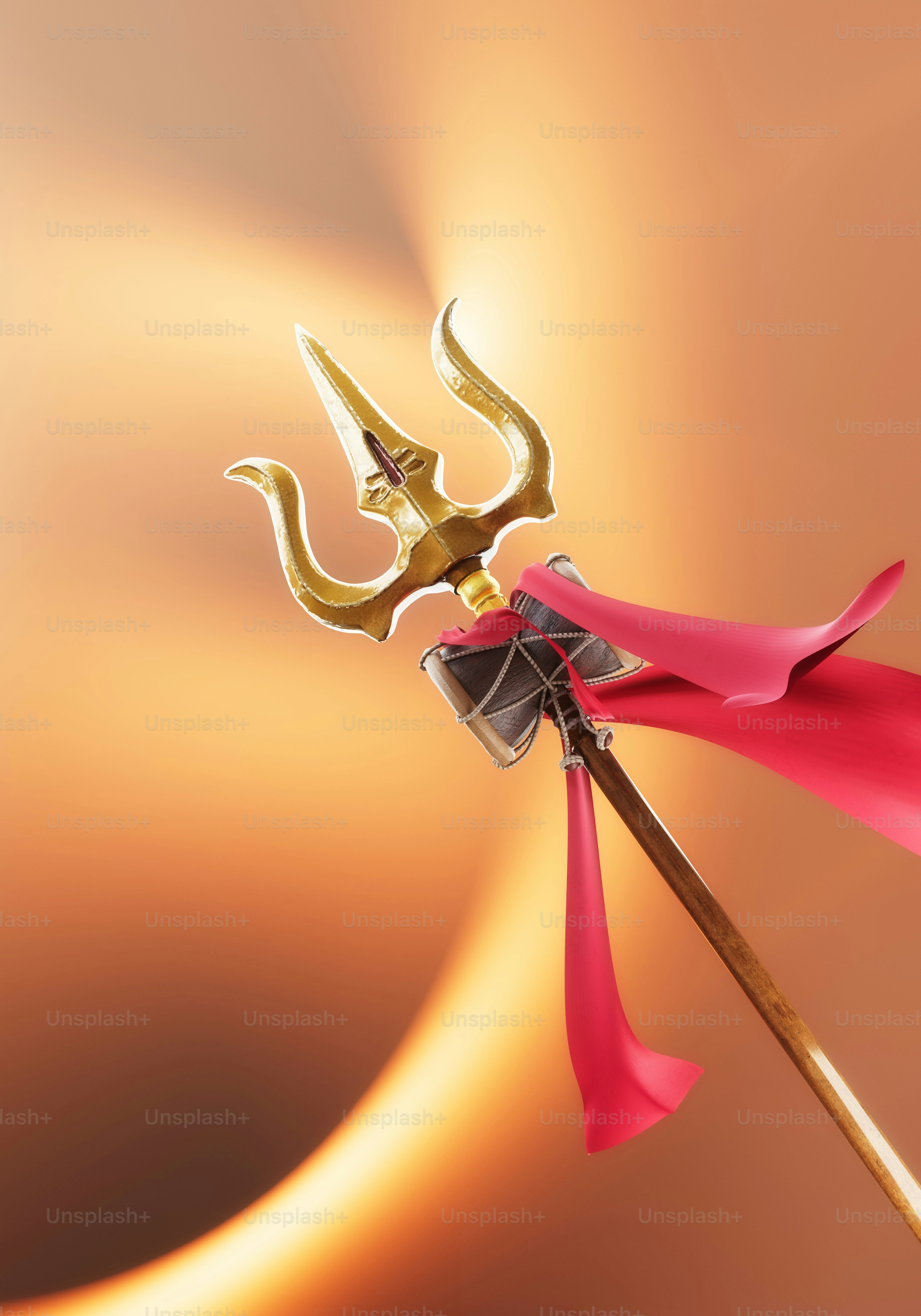 A golden trident with a small drum and red fabric against a warm background