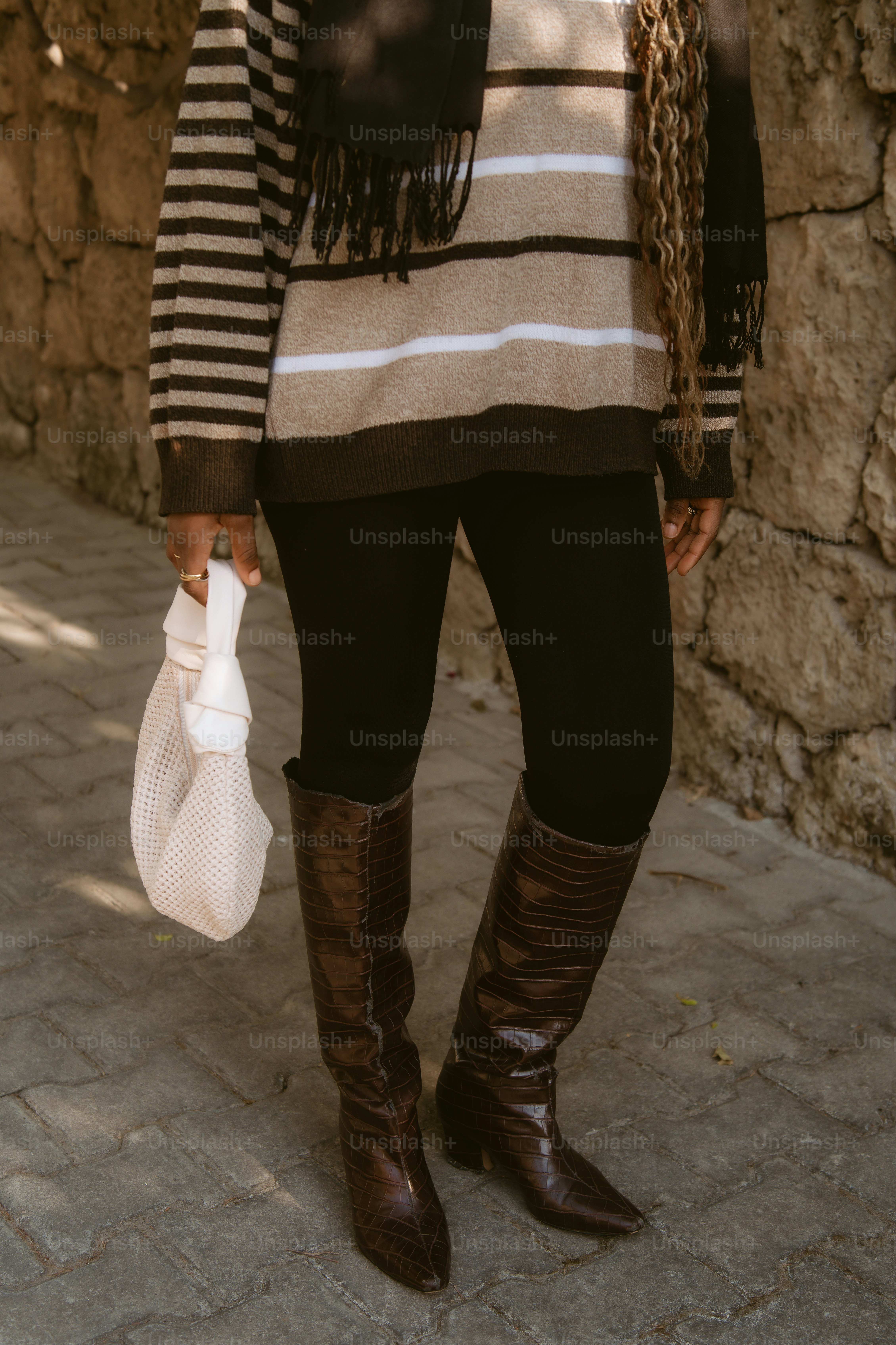A person in a striped sweater and black leggings holding a white bag